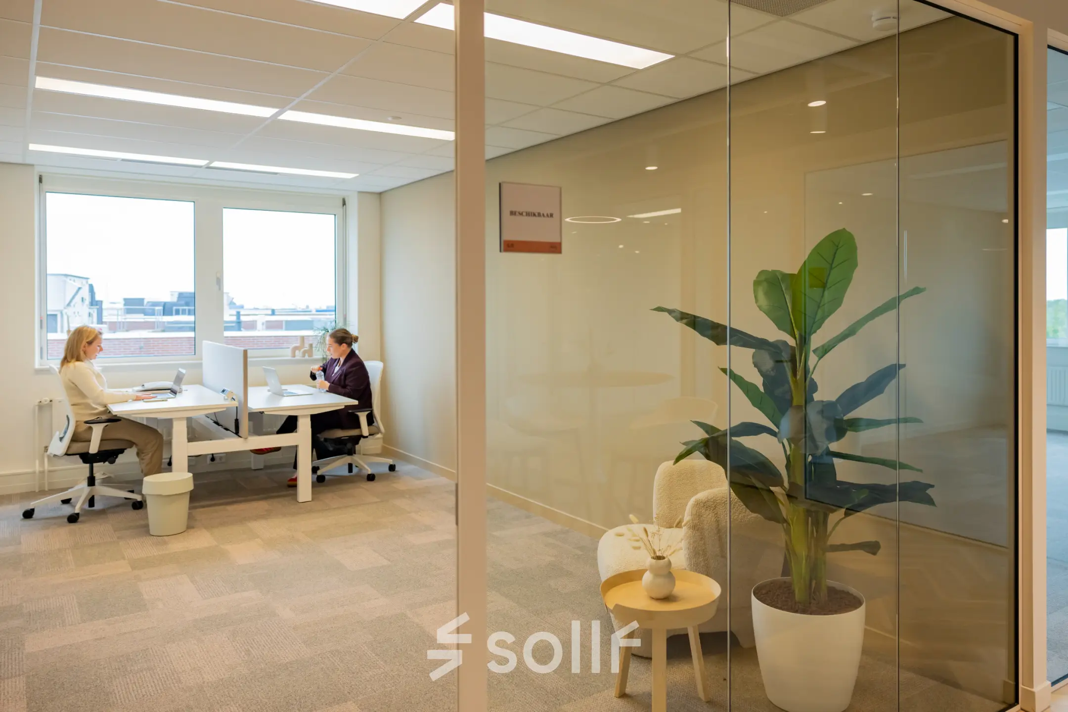 Heldere kantoorruimte op Baron van Nagellstraat 136, Barneveld, met moderne werkplekken en uitzicht. Twee mensen zijn aan het werk.