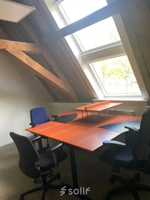 Kantoorruimte op Blokstallen 2B, Bergen op Zoom met een houten dak en grote ramen. Meubels met meerdere bureaus en stoelen zijn zichtbaar, ideaal voor kantoorruimte huren.