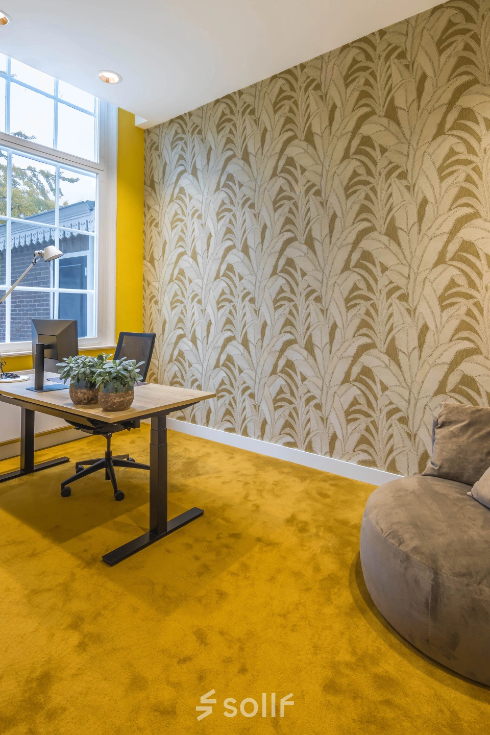 Kantoorruimte huren met geel tapijt en opvallende printbehang op de muur, bureau met stoelen en plantdecoratie, raam biedt natuurlijk licht in het pand aan de Catharinastraat 16 in Breda Centrum-Station.
