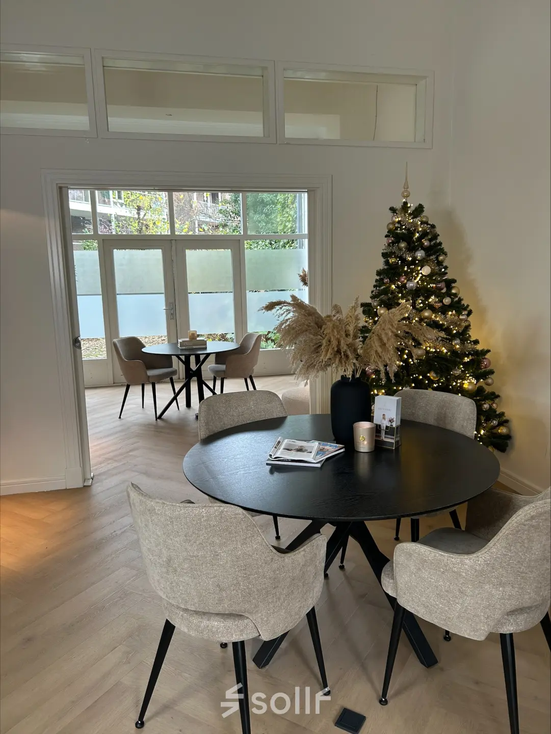Gezellige kantoorruimte in Breda met kerstboom en ronde tafel, perfect voor vergaderingen. Veel natuurlijk licht en uitzicht op een patio. Ideaal voor kantoorruimte huren tijdens de feestdagen.