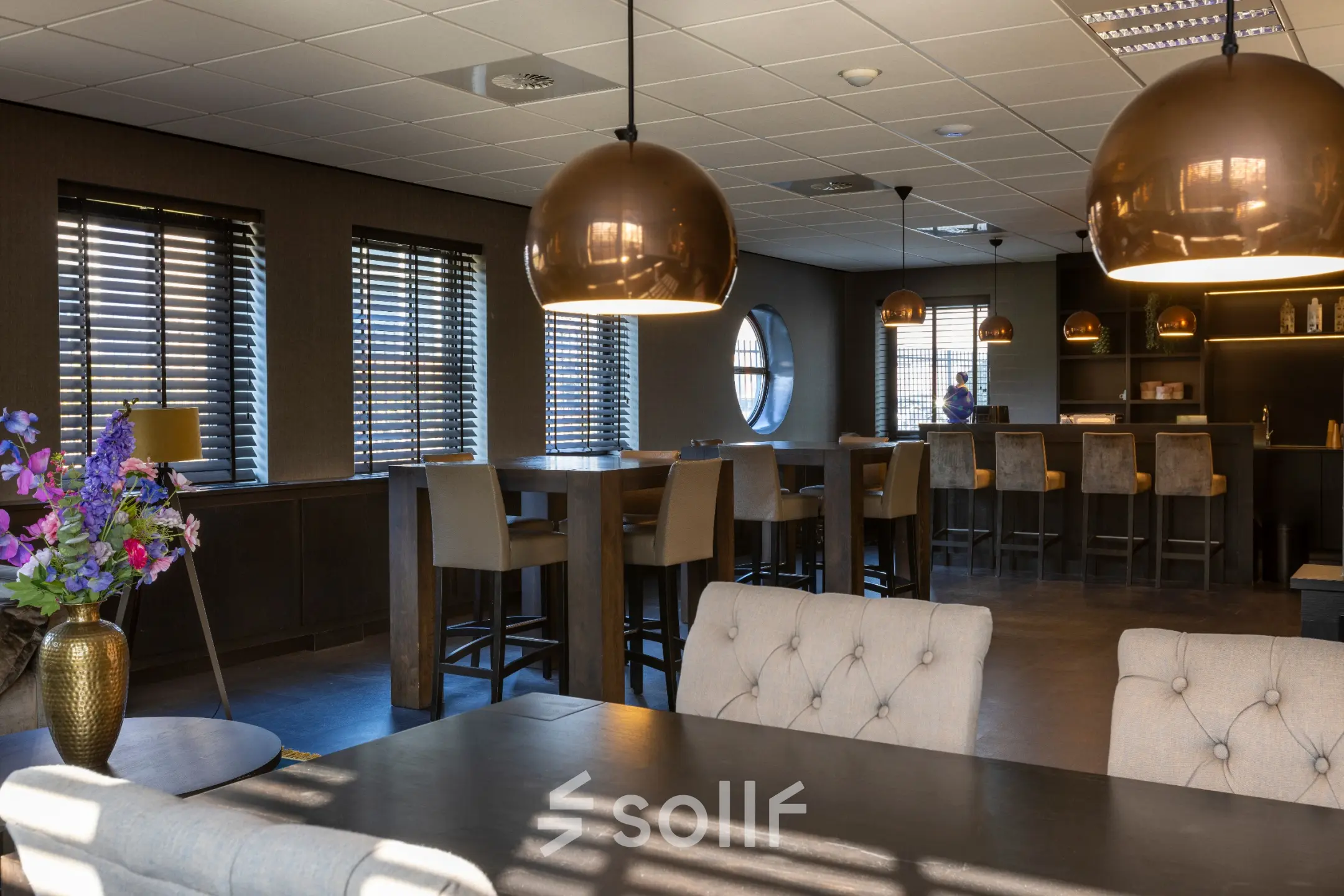 Moderne kantoorruimte huren in kantoorpand aan Takkebijster 57A, Breda Oost-Brabantpark. Gemeubileerd interieur met hoge tafels, barkrukken en ronde lampen, perfect voor een open werkomgeving.