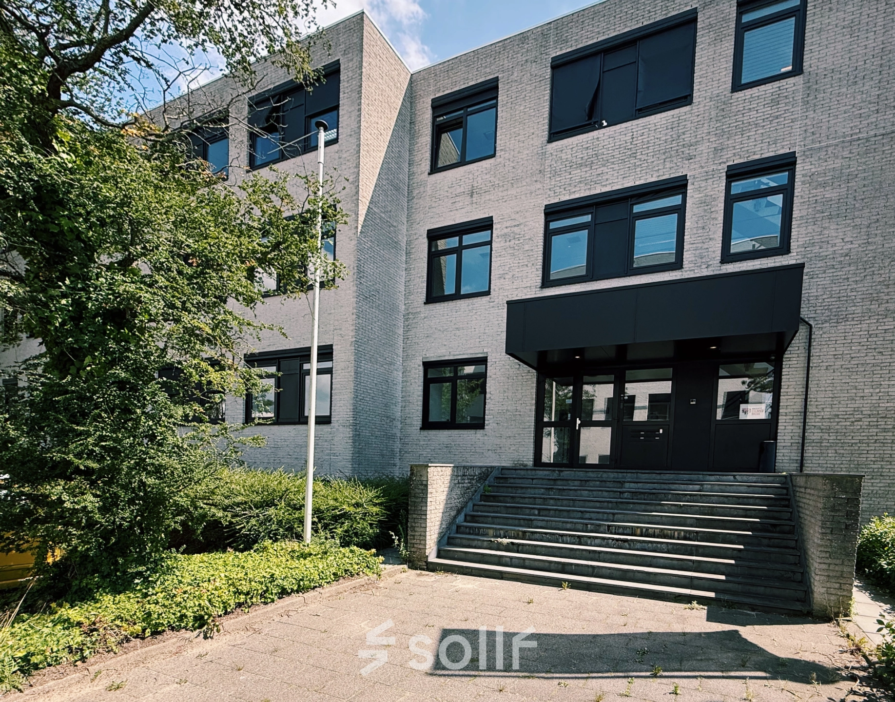 Het kantoorpand aan de Druivenstraat 25-31 in Breda Oost, geschikt voor kantoorruimte huren. De moderne gevel met grote ramen is omgeven door groen en betegelde paden.