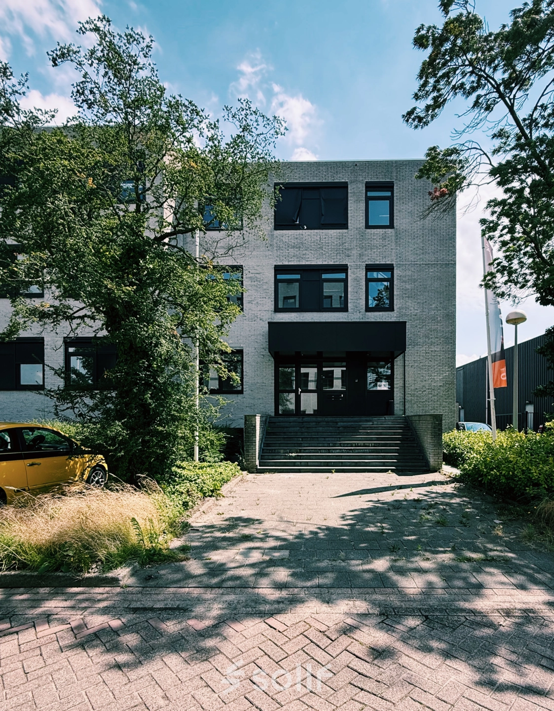 Entree van kantoorpand aan de Druivenstraat 25-31 in Breda Oost, met bomen en een geparkeerde auto voor de ingang.