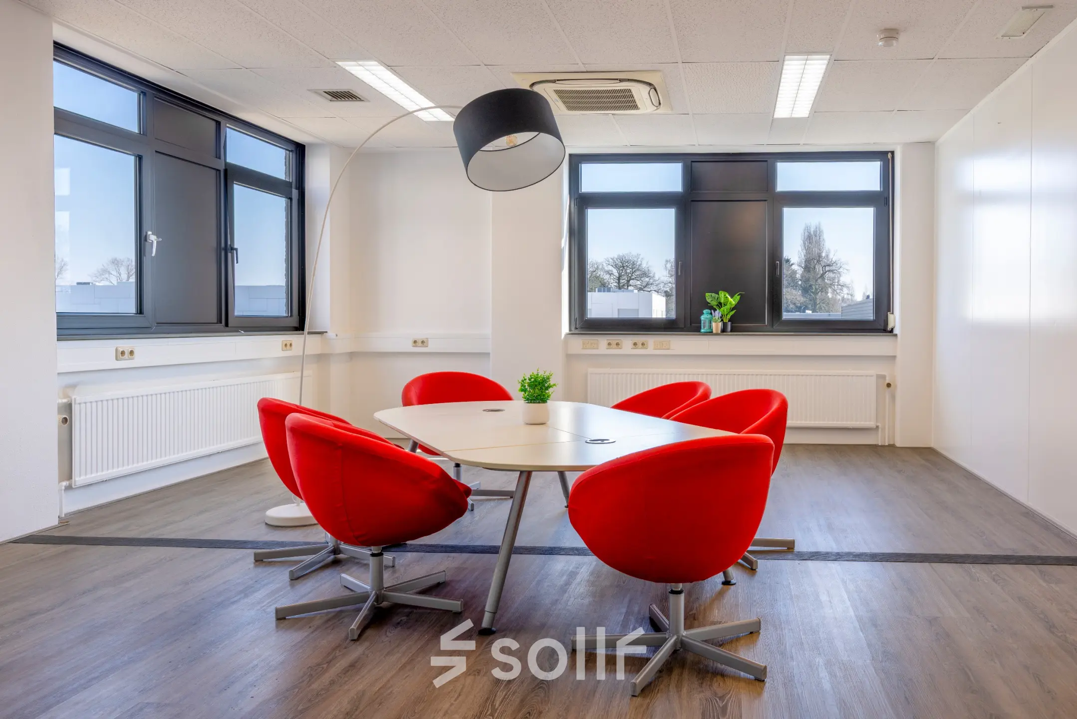 Vergaderruimte in kantoorpand Druivenstraat 25-31, Breda Oost, met rode stoelen rond een ovale tafel. Veel lichtinval door grote ramen. Geschikt voor kantoorruimte huren.