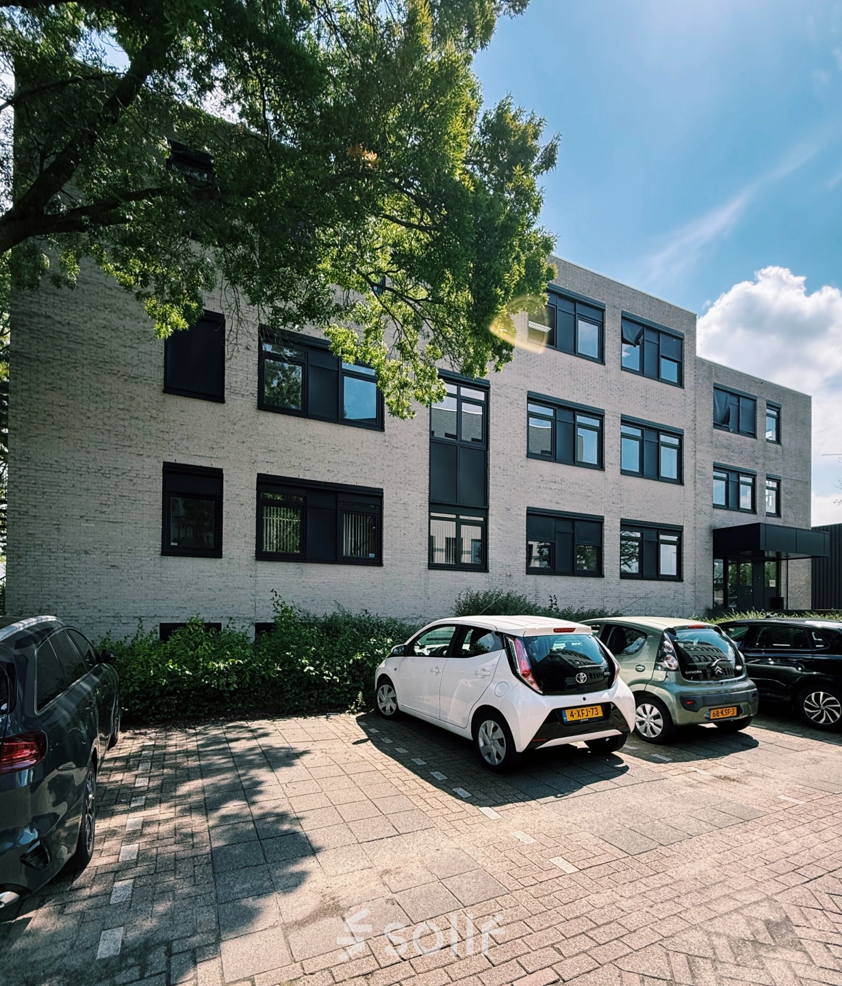 Kantoorruimte huren in Breda Oost aan de Druivenstraat 25-31, met een modern kantoorpand en enkele geparkeerde auto's op de voorgrond.