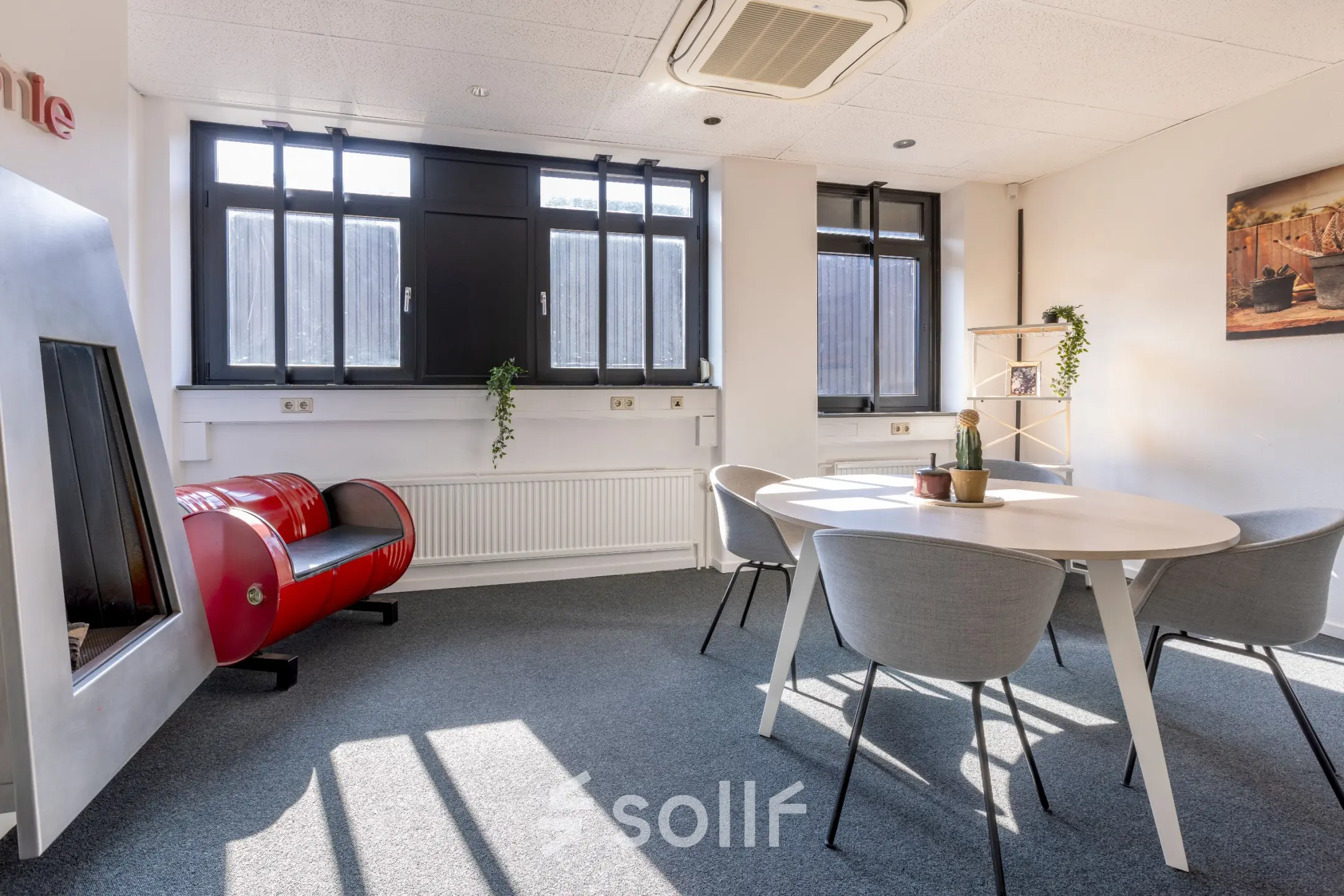Lichte kantoorruimte met grote ramen, ronde tafel met stoelen en een decoratieve open haard in kantoorpand op Druivenstraat 25-31, Breda Oost. Ideaal voor kantoorruimte huren.