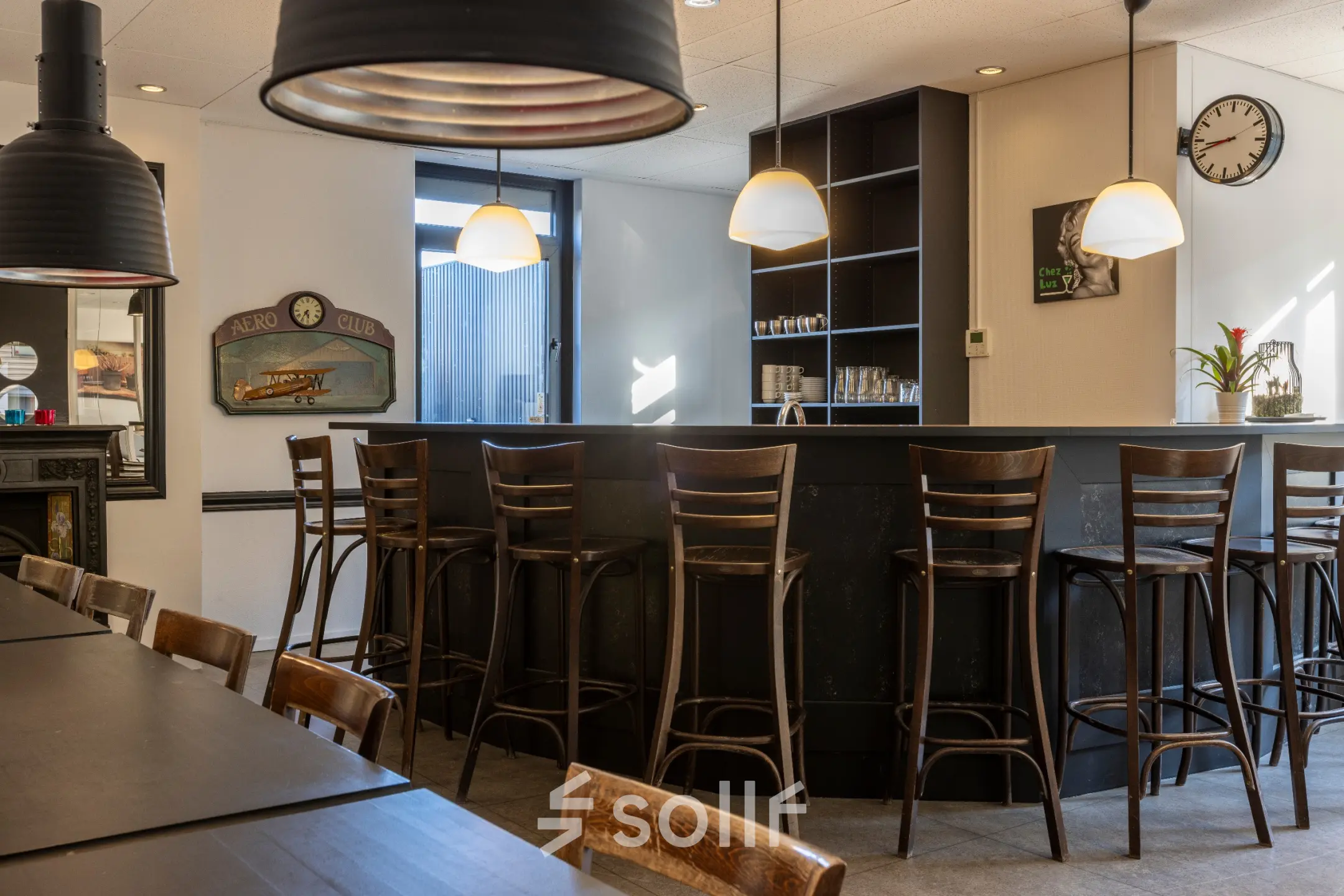 Een moderne kantoorruimte te huur in Breda Oost aan de Druivenstraat 25-31. Het interieur is voorzien van hoge houten stoelen aan een bar en een tafel. De ruimte is uitnodigend en functioneel.