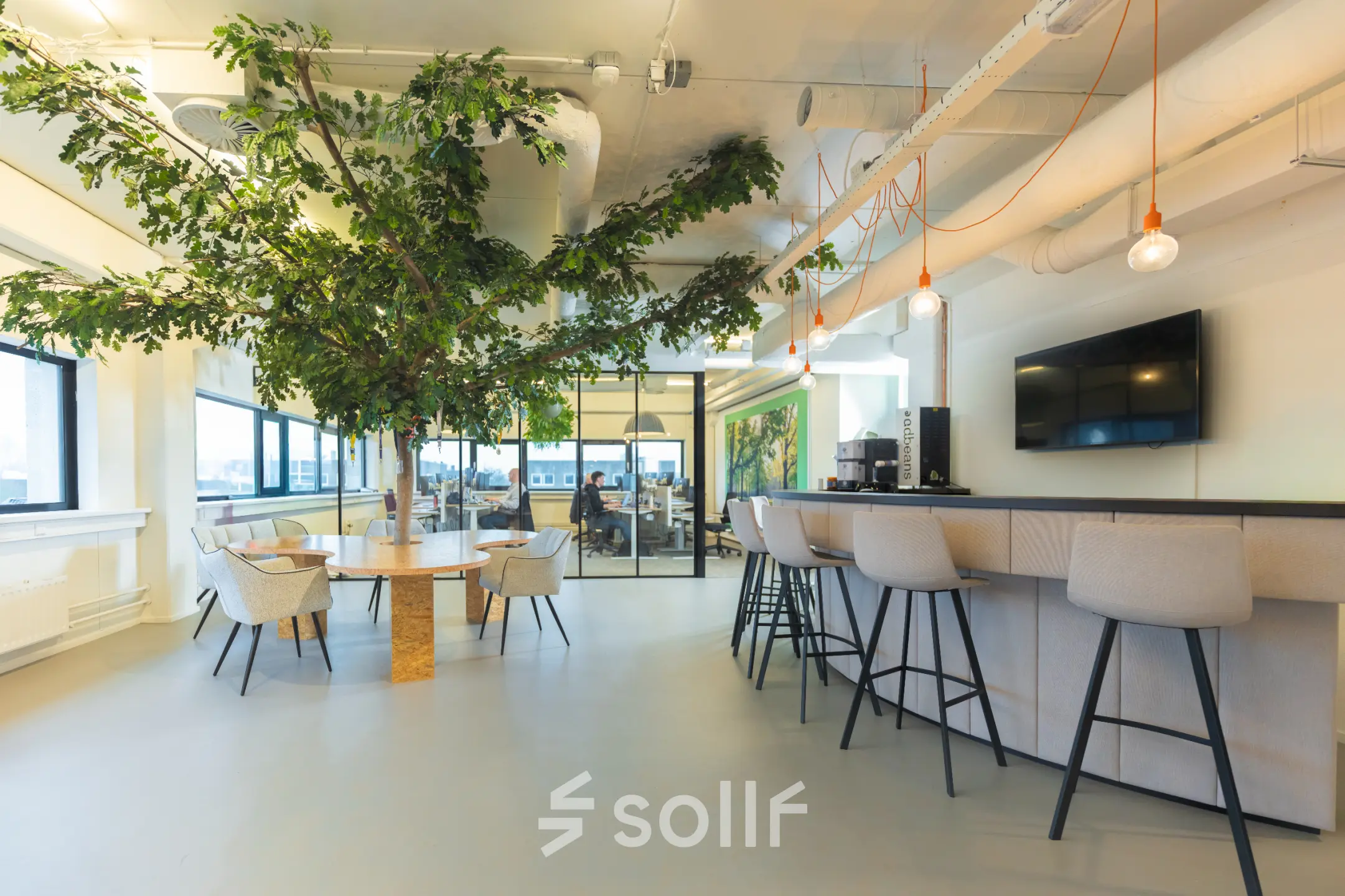 Moderne kantoorruimte op Rietbaan 2-12 in Capelle aan den IJssel, met een grote plant, stijlvolle zithoek en bar met krukken. Perfect om te huren voor zakelijke bijeenkomsten.