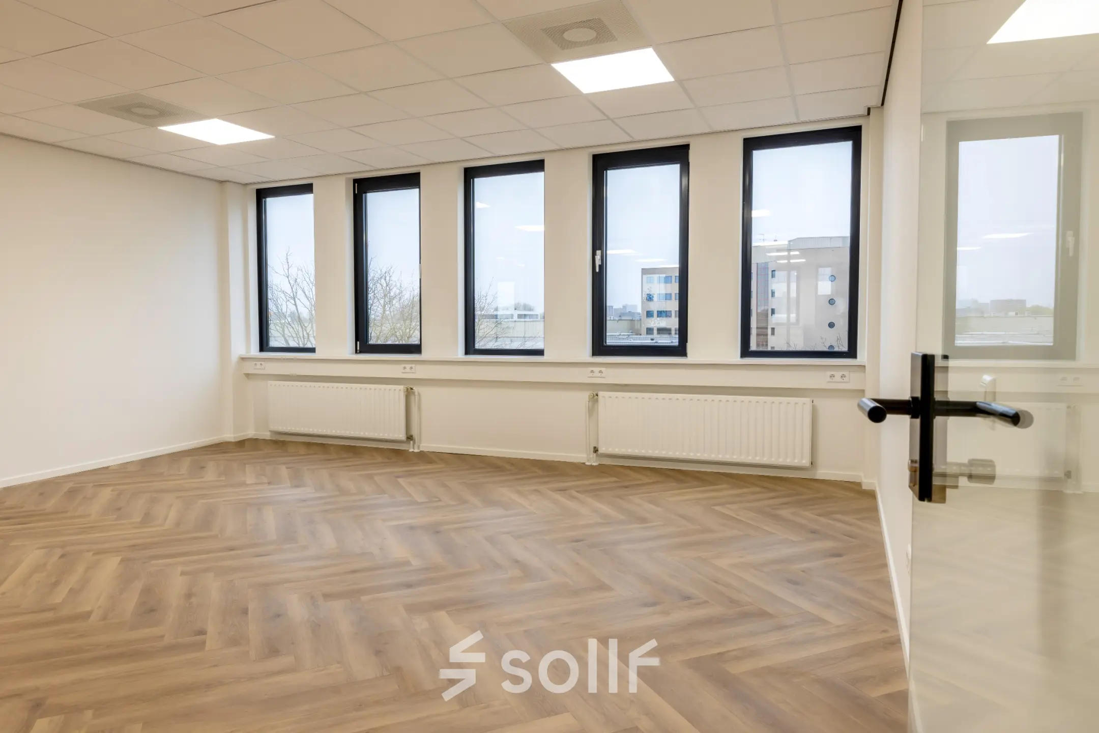 Lichte kantoorruimte aan Vlierbaan 20, Capelle aan den IJssel, met grote ramen voor natuurlijk licht, ideaal voor huur. Houten vloer in visgraatpatroon geeft het kantoorpand een stijlvolle touch.