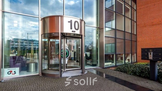 Hoofdingang van het kantoorpand op Olof Palmerstraat 10 in Delft met grote glazen gevel en draaideur, perfect voor diegene die kantoorruimte wil huren in een moderne omgeving.