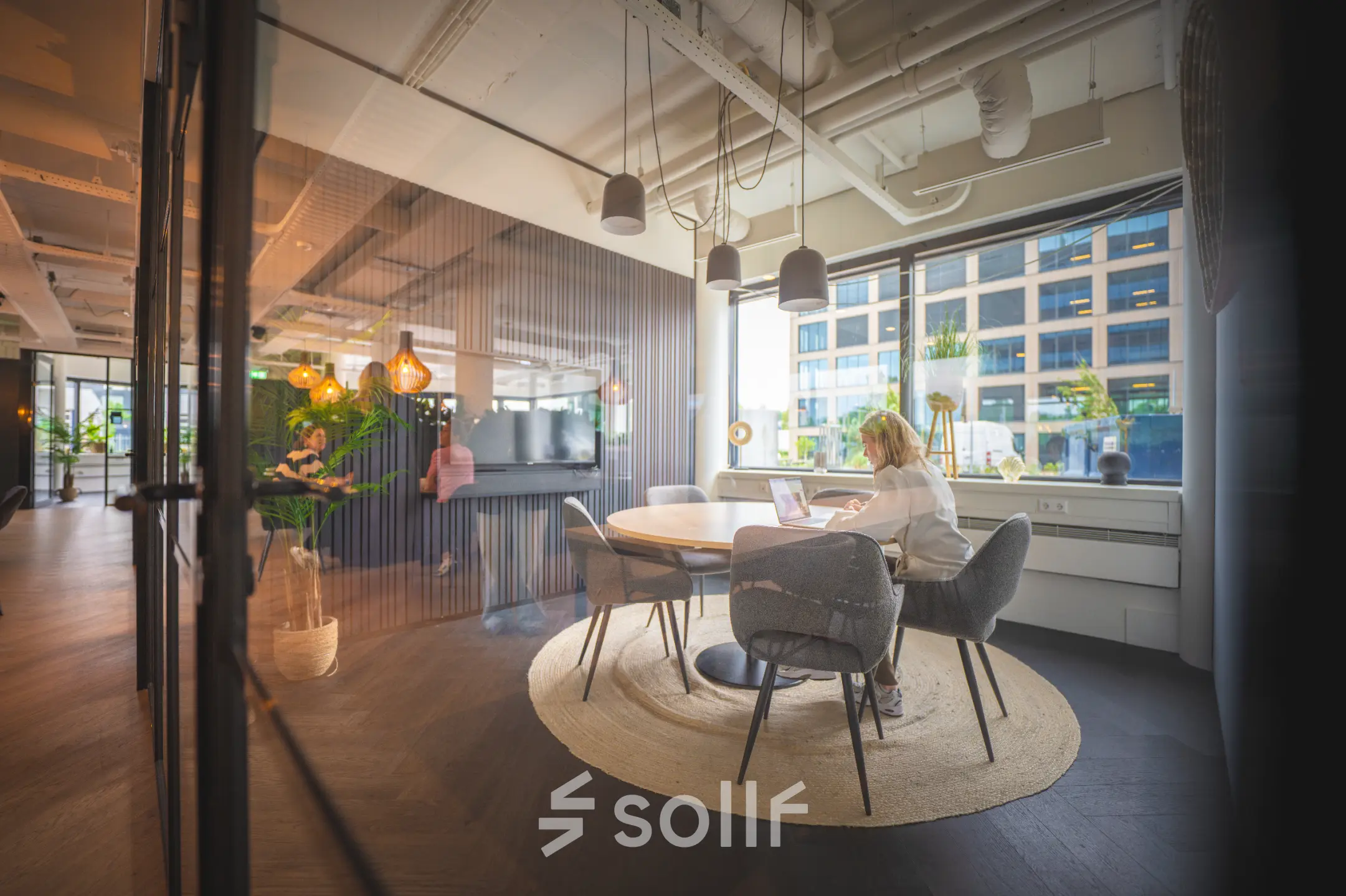 Moderne kantoorruimte huren in Den Bosch met een lichte vergaderruimte, voorzien van ronde tafel en comfortabele stoelen. Mensen aan het werk op laptops, met grote ramen voor natuurlijk licht.