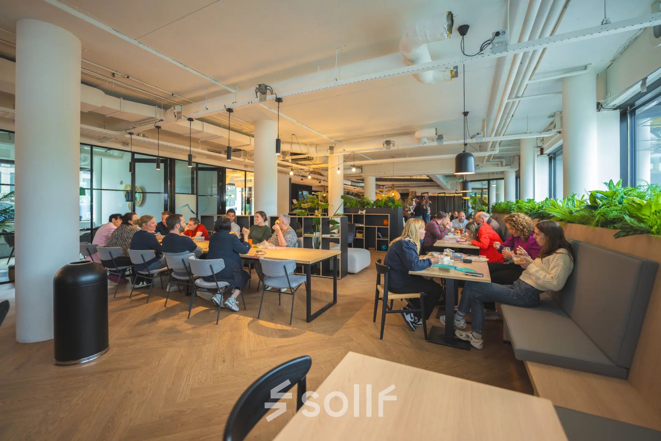 Kantoorruimte huren in Den Bosch met een moderne, gemeubileerde open werkvloer op Hambakenwetering 1, waar mensen geconcentreerd samenwerken en brainstormen aan tafels.