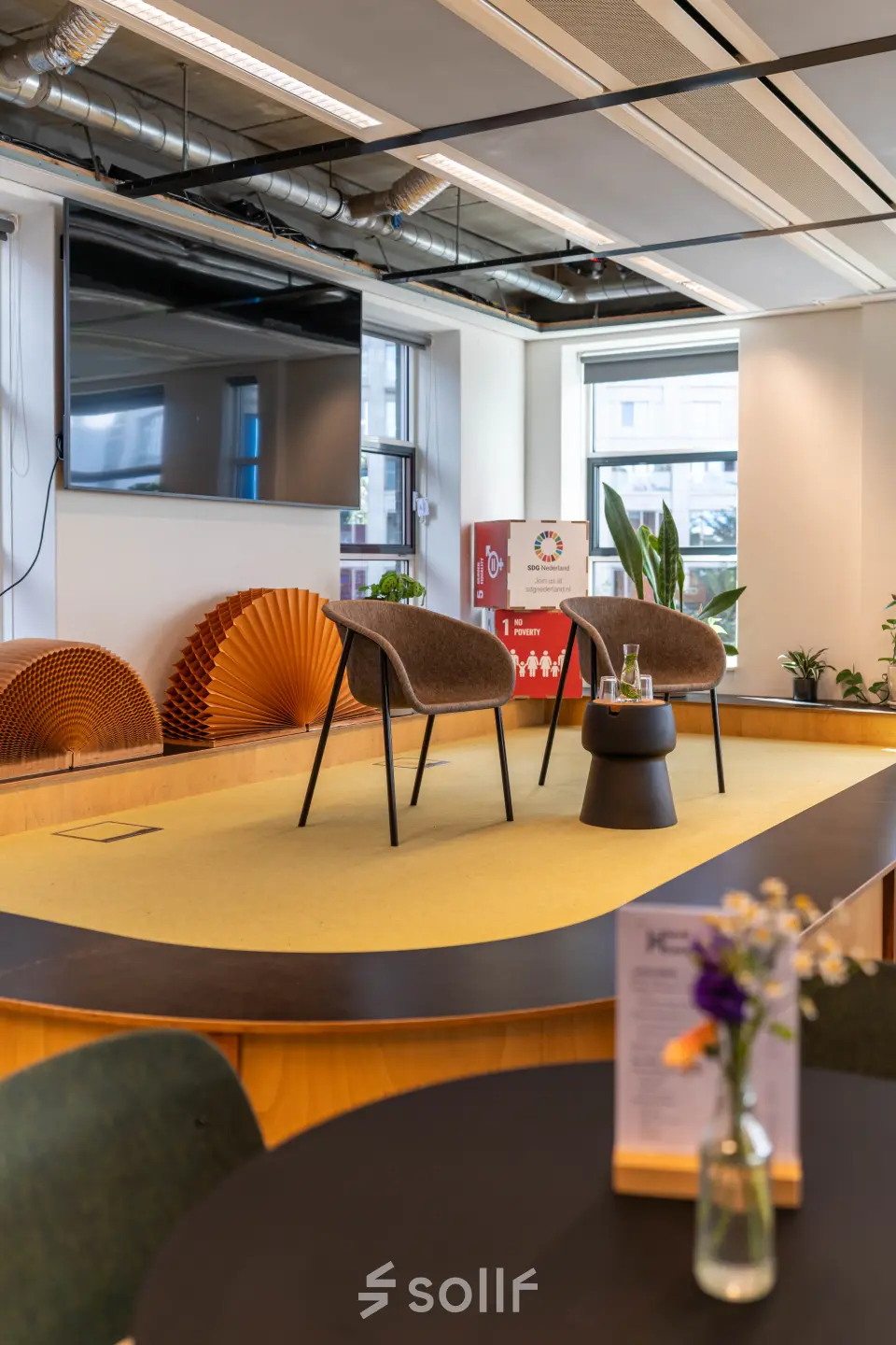 Moderne kantoorruimte te huur op Fluwelen Burgwal 58 in Den Haag Centrum, met een podium, stoelen, en planten op de achtergrond.