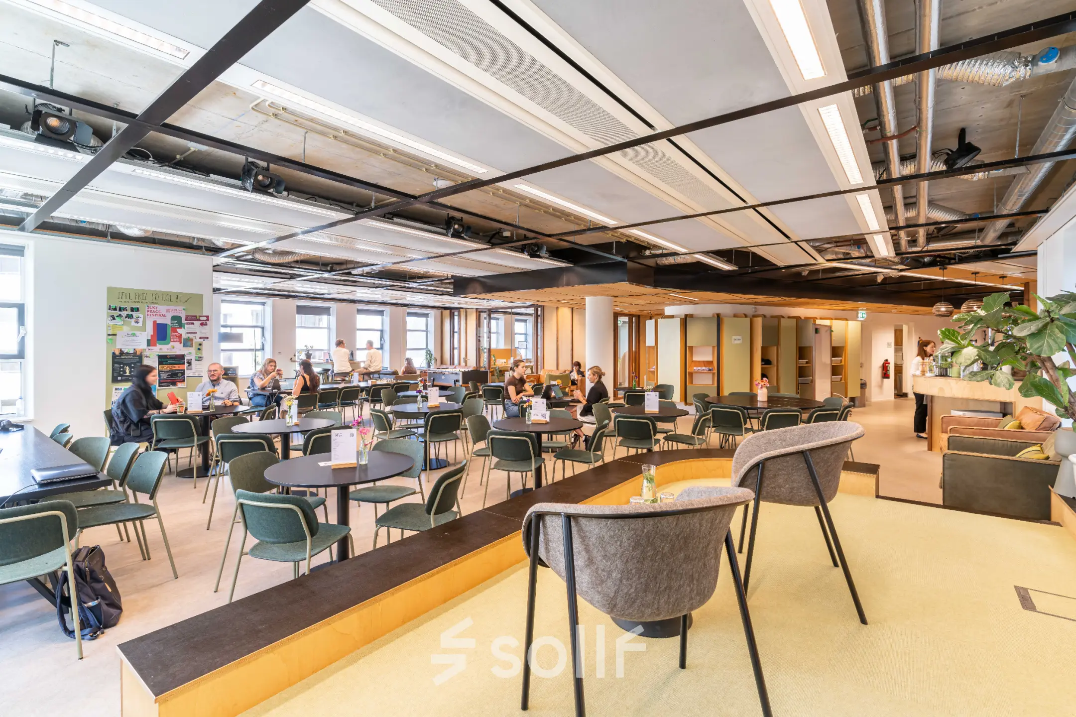 Lichte kantoorruimte in Den Haag Centrum met moderne inrichting en werkende mensen aan tafels. Ideaal voor het huren van een dynamische werkplek.