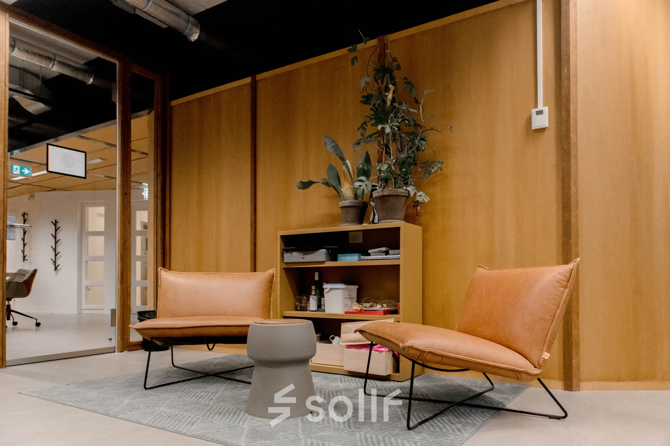 Kantoorruimte Fluwelen Burgwal 58, Den Haag Centrum, met twee leren stoelen, een houten wand en een plant, geschikt om als kantoor te huren.