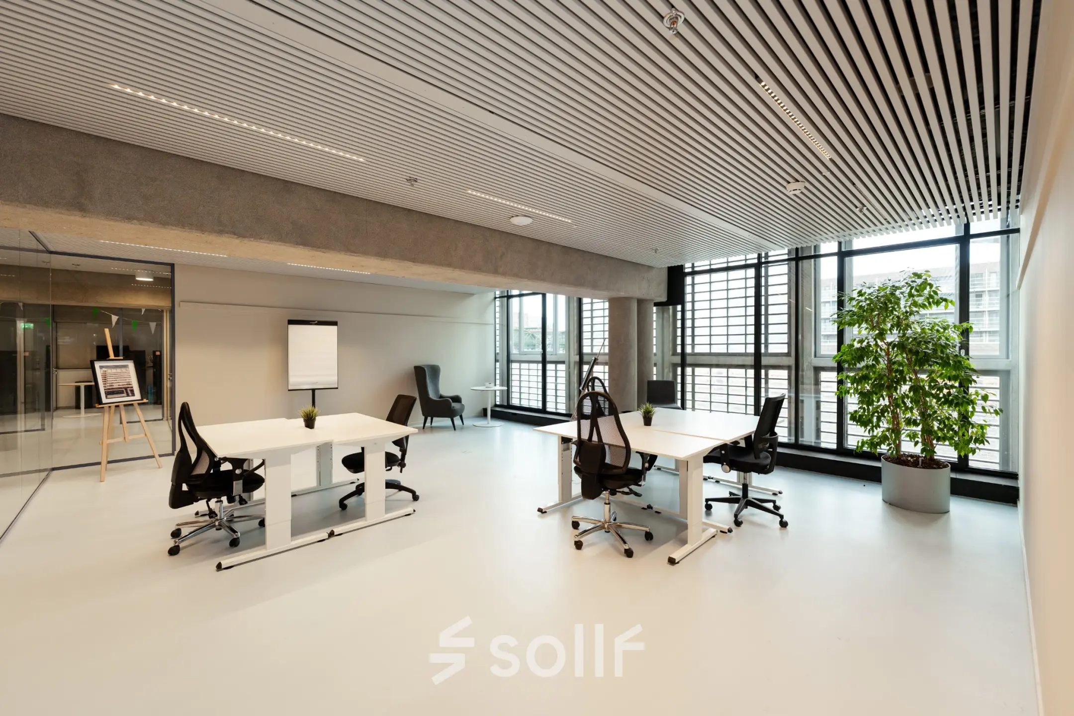 Moderne kantoorruimte te huur op Waldopstraat 5, Den Haag Centrum. Lichte werkruimte met grote ramen, twee bureaus met stoelen en een flipover, ideaal voor creatieve werkprocessen.