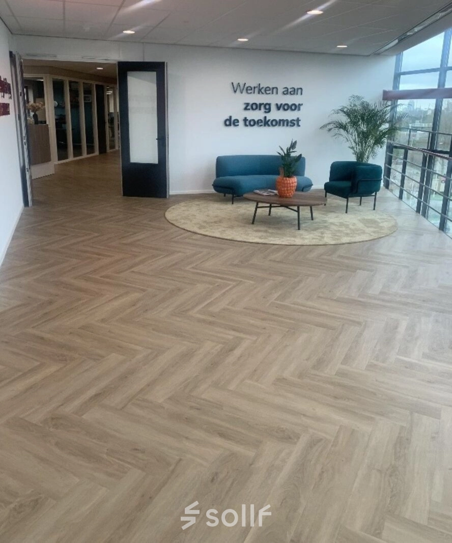Moderne kantoorruimte met houten vloer, twee blauwe fauteuils en een kleine bank aan Johan de Wittlaan 3-7, Den Haag Statenkwartier. Ruimte biedt volop licht en uitzicht voor bedrijven die kantoorruimte huren.