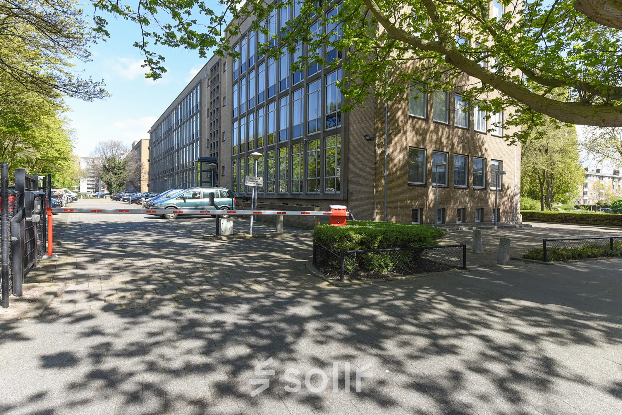 Exterieur van het kantoorpand aan de President Kennedylaan 19 in Den Haag Statenkwartier, met parkeerplaatsen en toegangsweg. Ideaal voor kantoorruimte huren in een groene omgeving nabij voorzieningen.