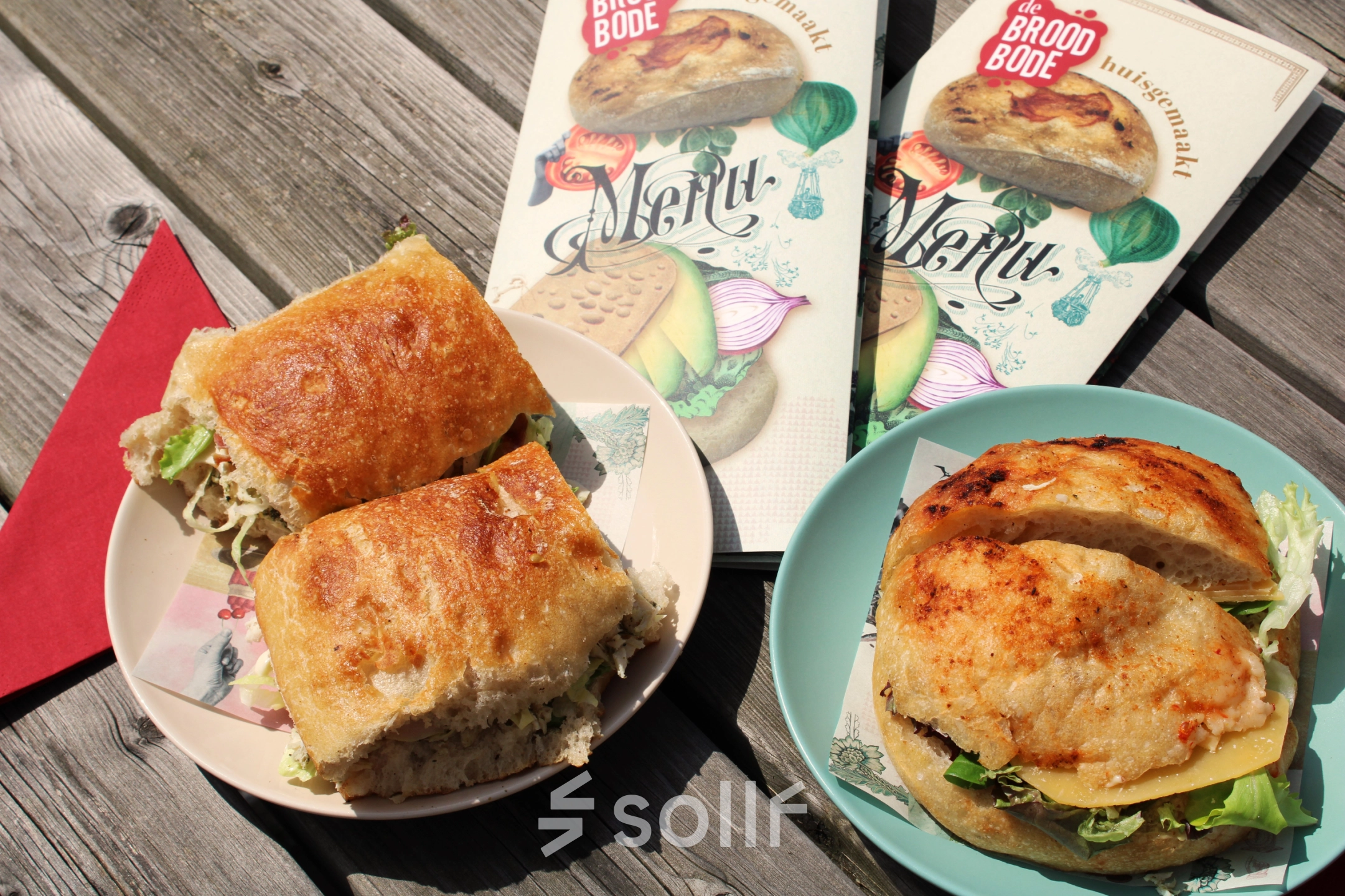 Zonnig terras met houten tafel en smakelijke lunchgerechten zoals broodjes van De Broodbode.