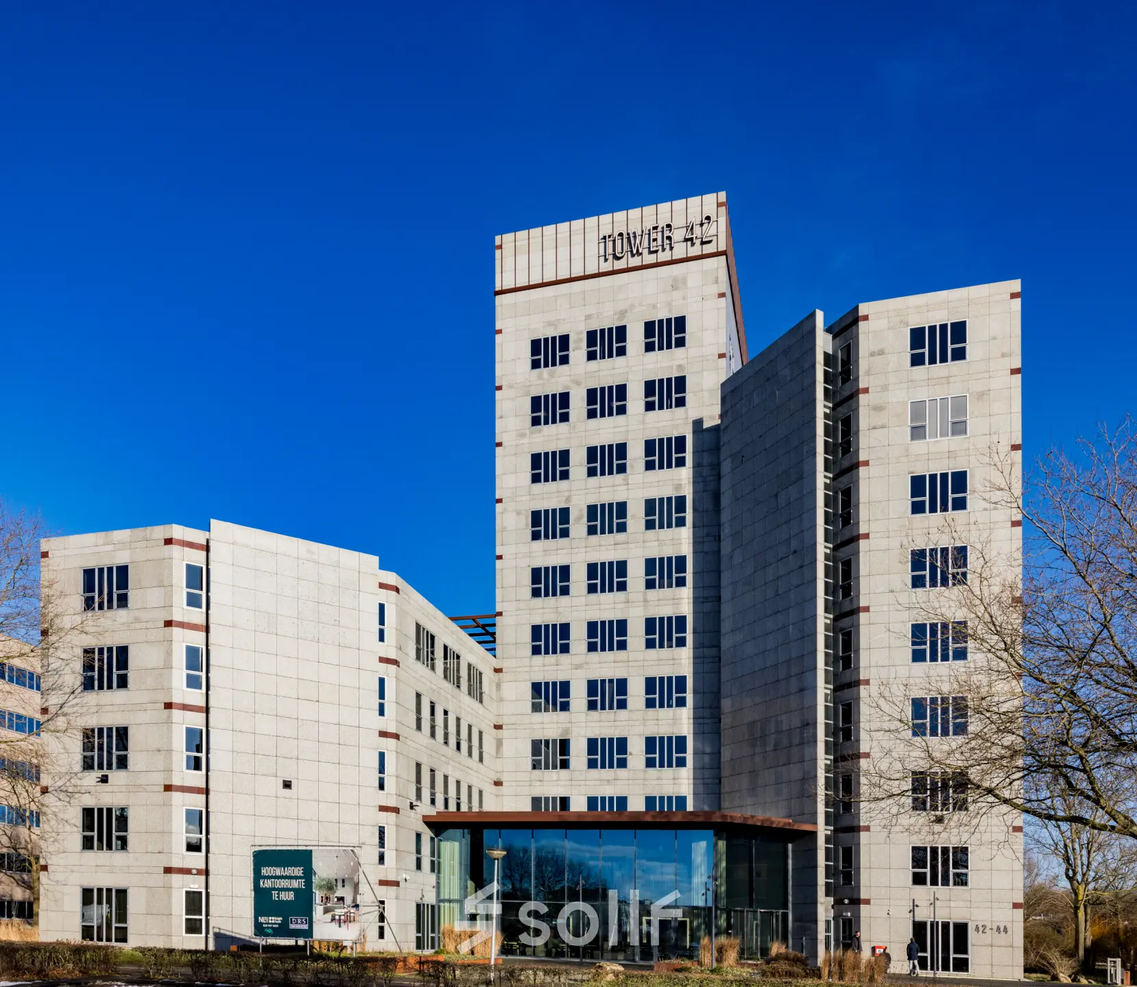 Modern kantoorpand op Diemerhof 42, Diemen, ideaal voor kantoorruimte huren. Hoog gebouw met glazen entree en witgrijze gevels tegen een heldere lucht.
