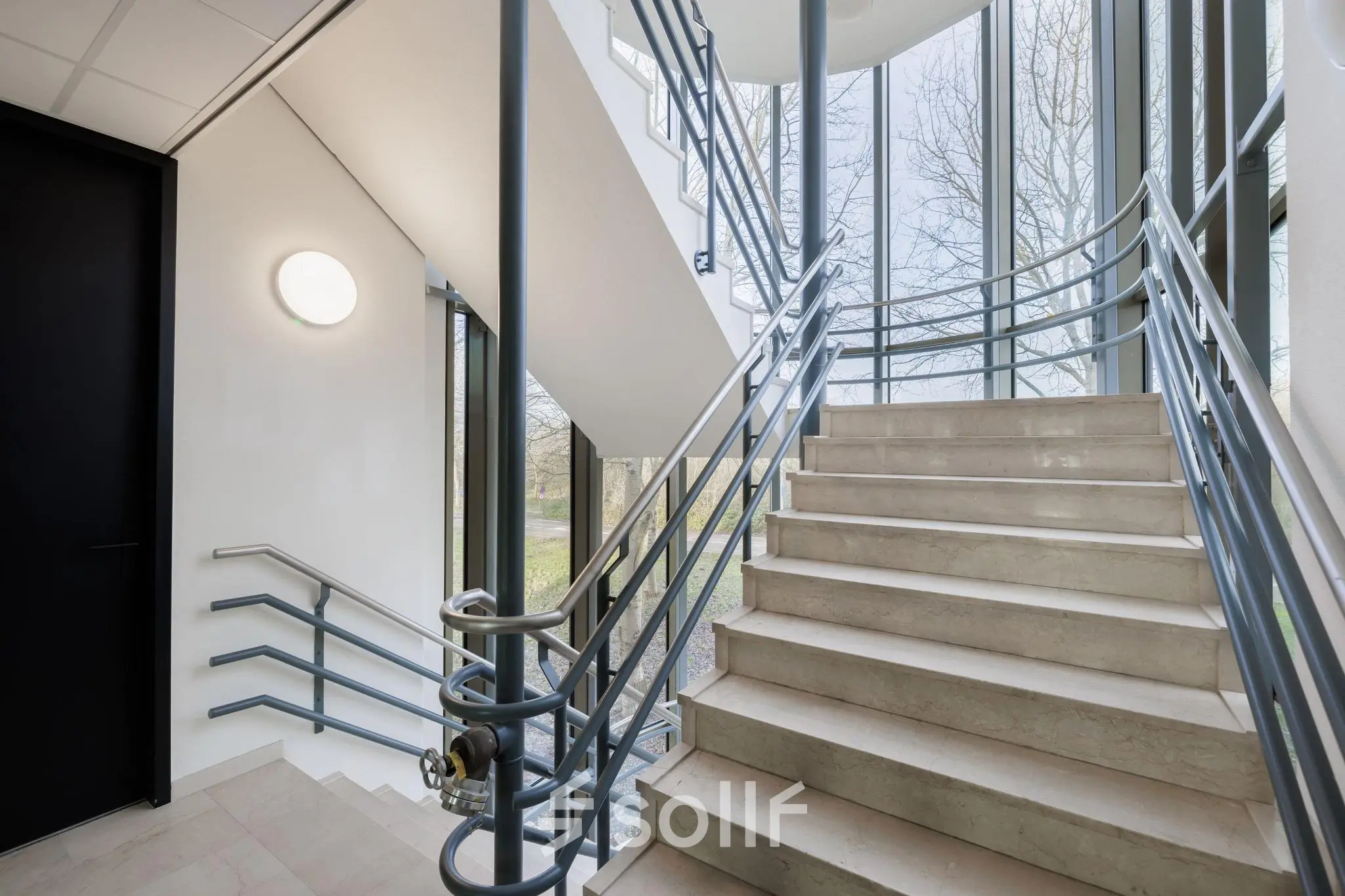 Entree met moderne trap in kantoorpand op Wisselwerking 40-48, Diemen, met uitzicht op groene omgeving en grote ramen voor veel natuurlijk licht. Geschikt voor kantoorruimte huren.