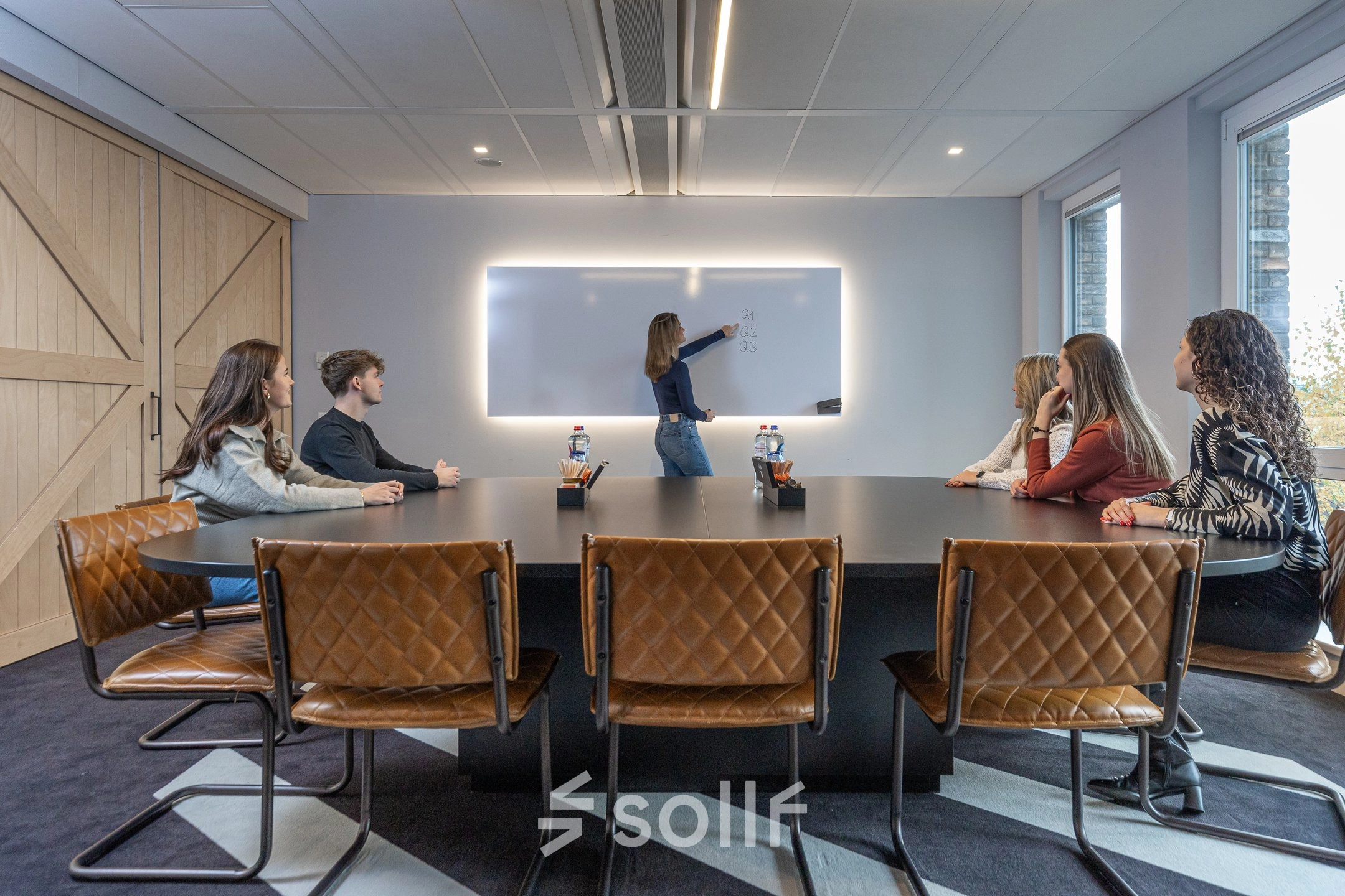Vergaderruimte in kantoorpand op Flight Forum 120-159, Eindhoven Airport, met zes personen aan tafel en een vrouw die presenteert bij een interactief bord. Kantoorruimte huren voor zakelijke bijeenkomsten.