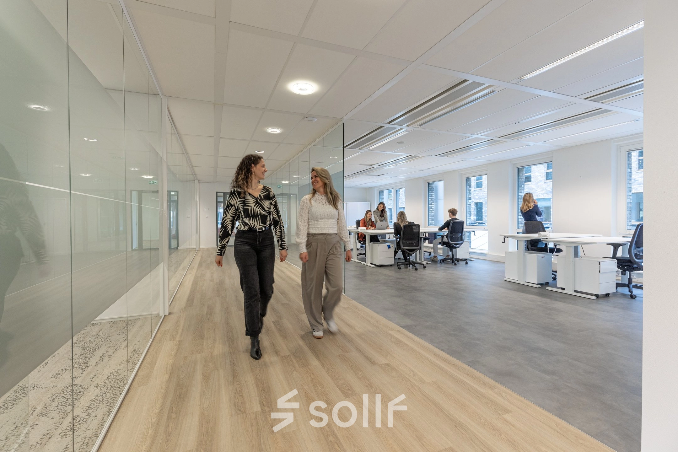 Moderne kantoorruimte huren bij Eindhoven Airport, Flight Forum 120-159. Ruime werkplekken met glazen scheidingswanden en aanwezigheid van medewerkers in overleg.