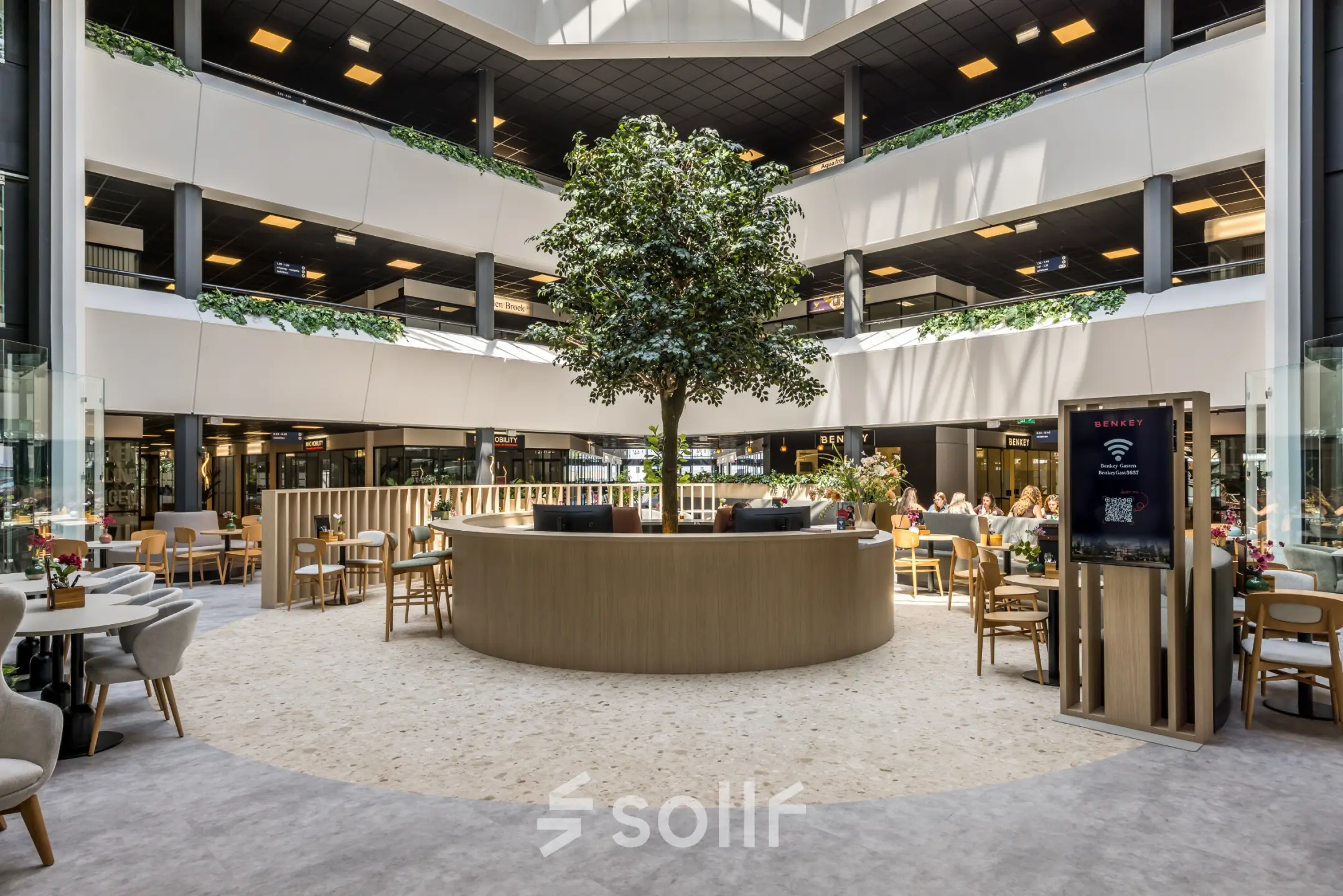 Moderne gemeubileerde kantoorruimte op Luchthavenweg 81, Eindhoven Airport, met een centraal geplaatste boom en mensen die aan tafels werken.