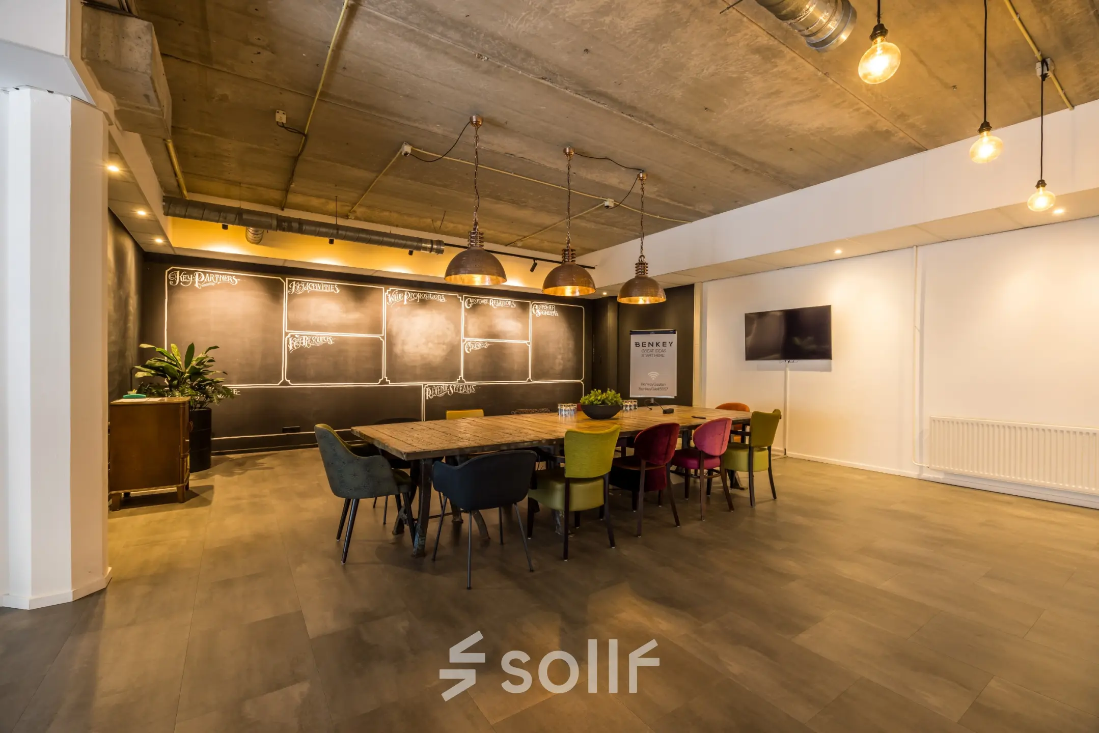 Stijlvolle vergaderzaal met lange houten tafel en gekleurde stoelen, ideaal voor kantoorruimte huren op Eindhoven Airport.