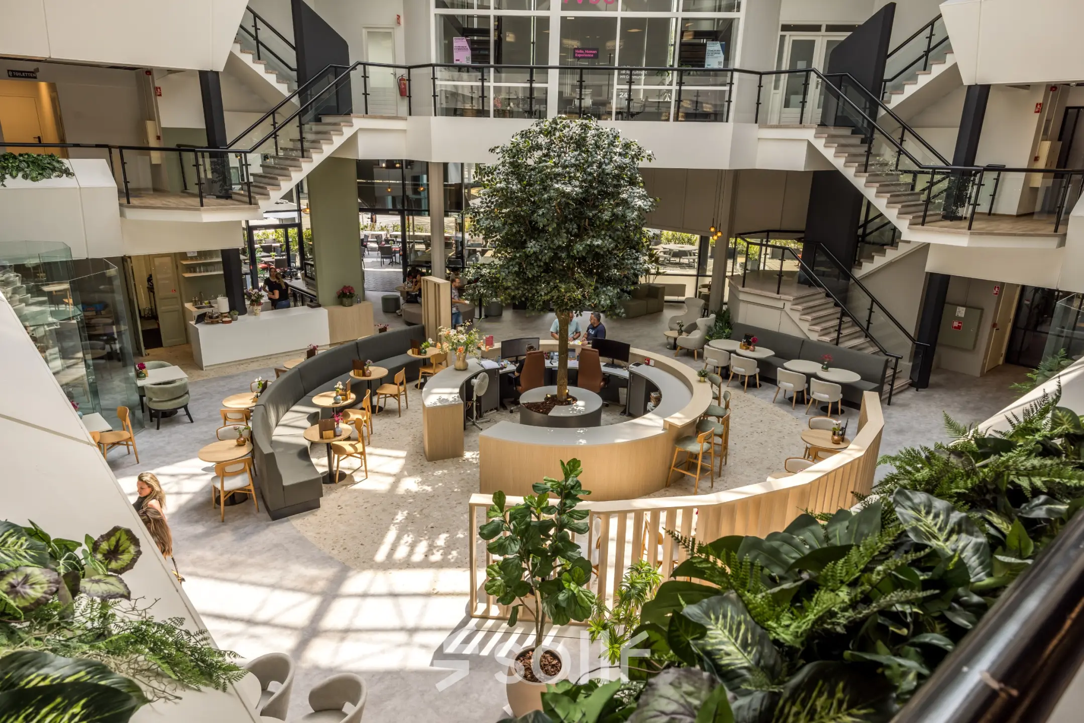 Moderne en open ingerichte lounge in een kantoorpand met veel groen en zitgelegenheid. Huur hier je kantoorruimte en geniet van een inspirerende omgeving aan de Luchthavenweg 81 in Eindhoven Airport.