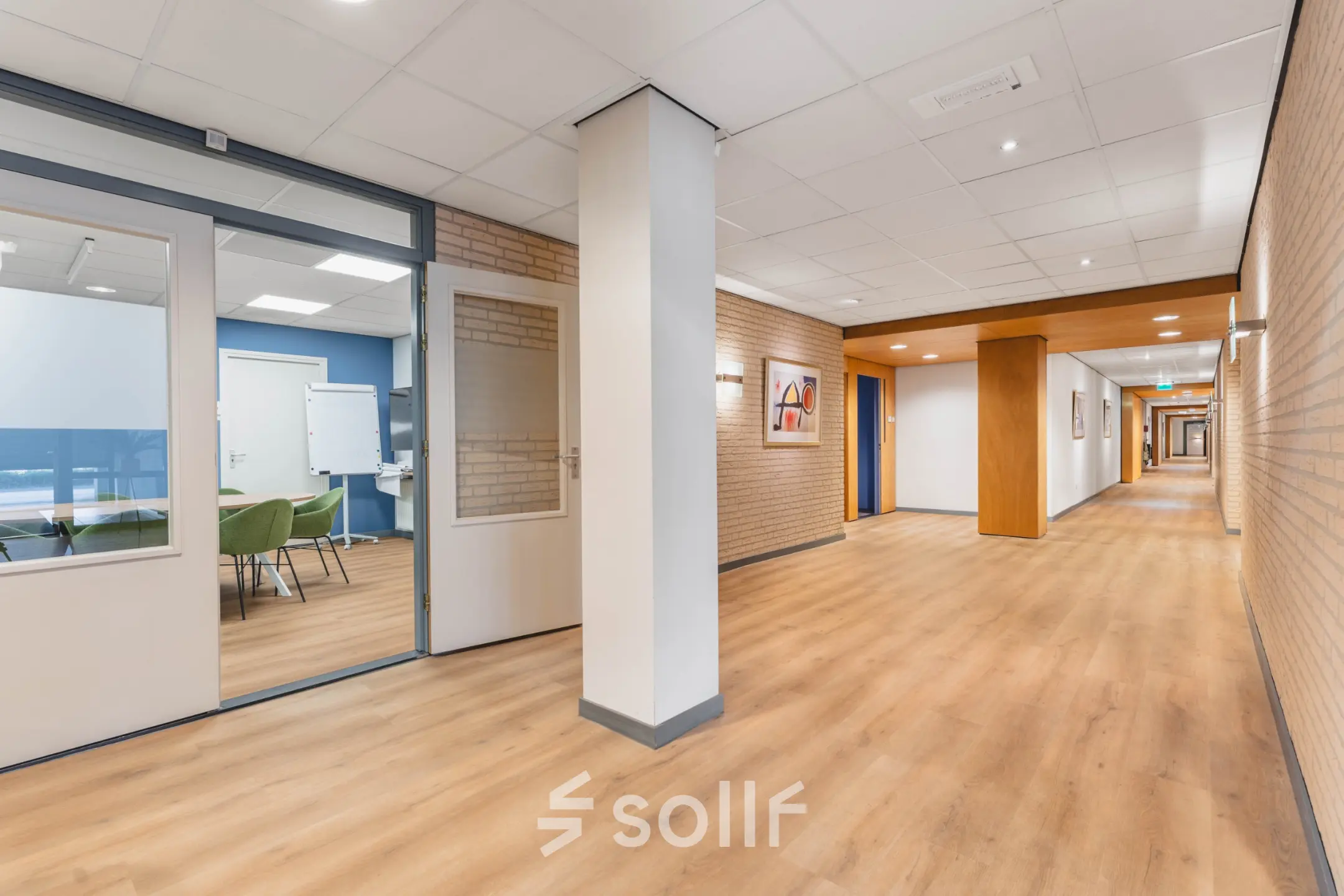 Heldere gang met houten vloer in kantoorpand op Kanaaldijk-Zuid 19, Eindhoven Centrum. Links een vergaderruimte met glazen deuren en modern interieur. Ideale plek voor kantoorruimte huren.
