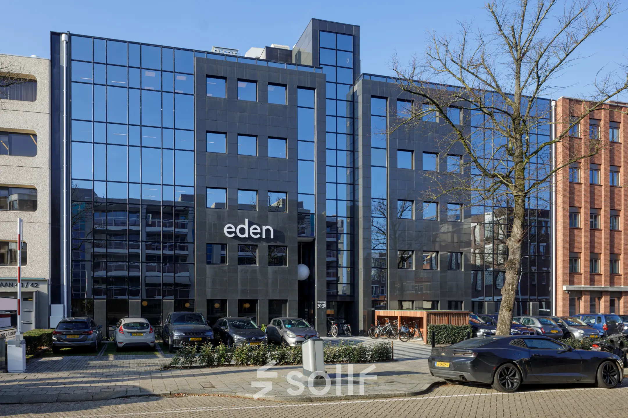 Glazen en moderne uitstraling van het kantoorpand aan de Paradijslaan 30-38 in Eindhoven Centrum, omringd door geparkeerde auto's. Ideale locatie voor het huren van kantoorruimte.