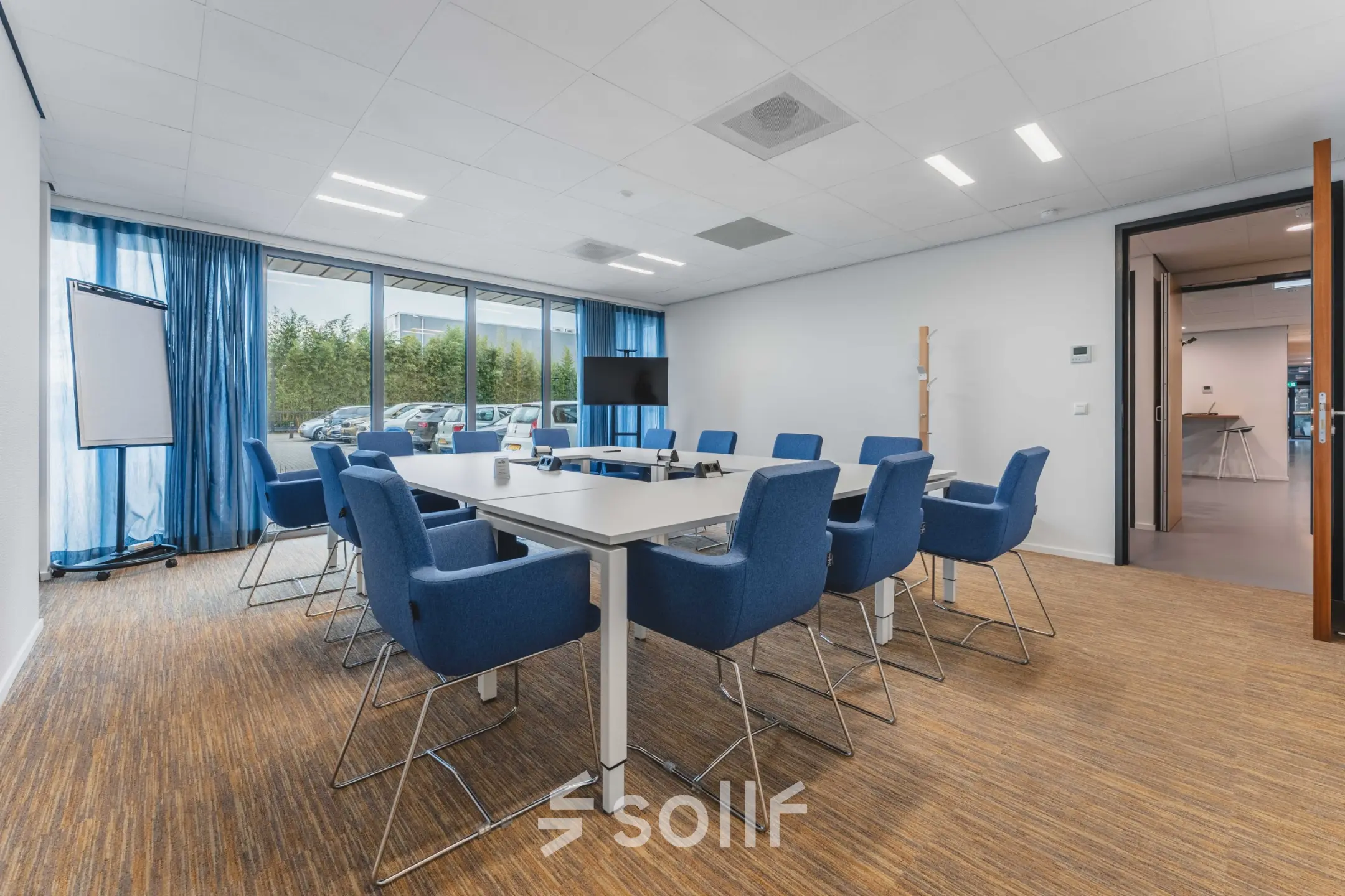 Vergaderruimte met grote tafel en blauwe stoelen, perfect voor kantoorruimte huren op Hurksestraat 60 in Eindhoven De Hurk. Ruime kantoorpandomgeving met moderne faciliteiten voor zakelijke bijeenkomsten.