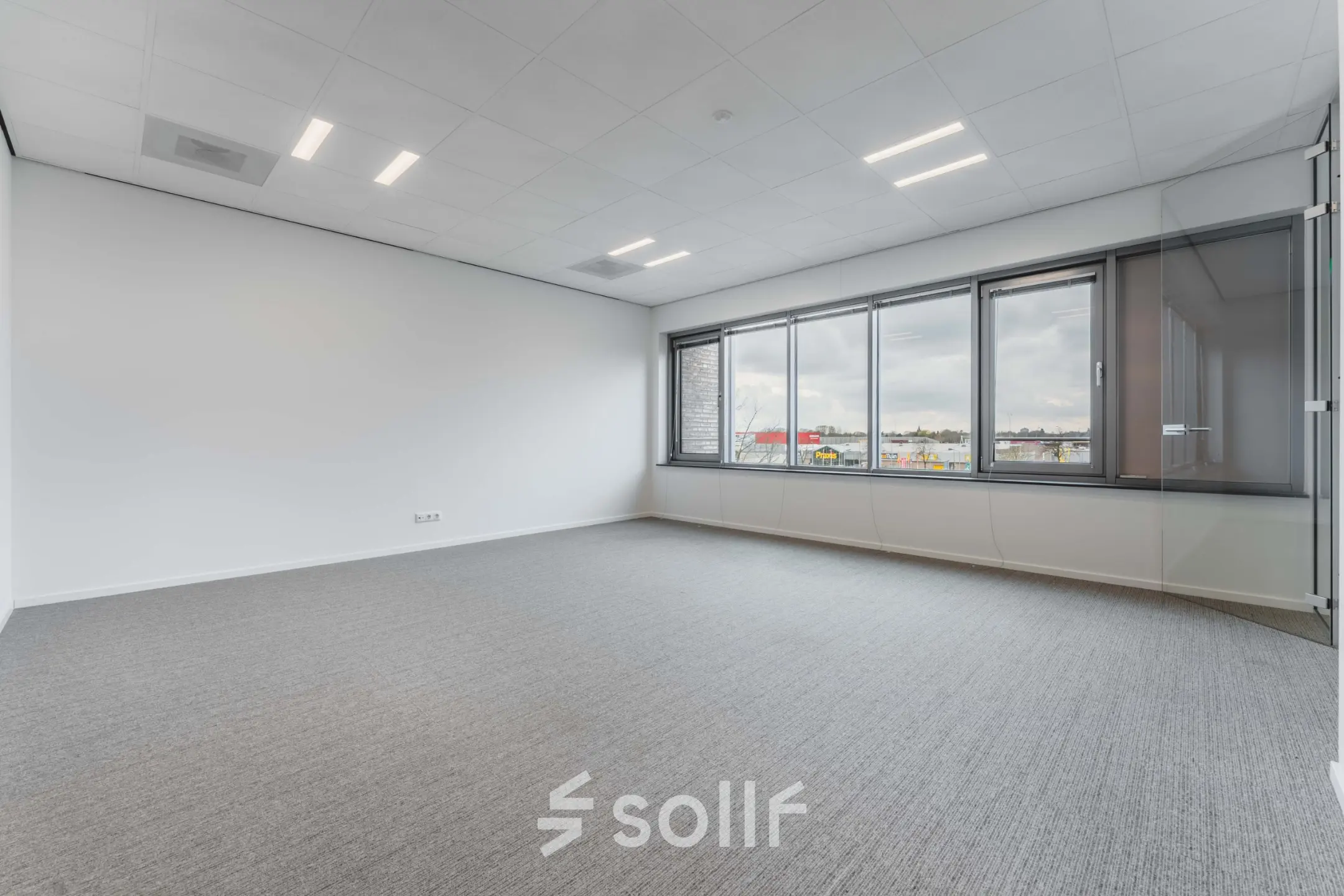 Ruime, heldere kantoorruimte te huur in Eindhoven De Hurk met groot raam en grijze vloerbedekking, ideaal voor het inrichten van moderne kantoren.
