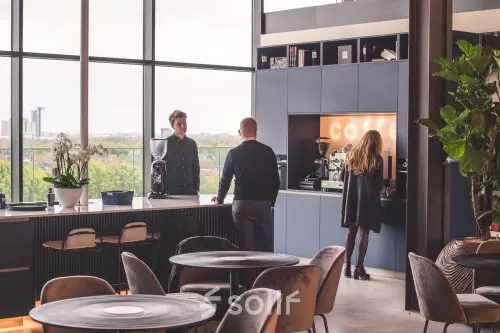 Gezellige kantineruimte in kantoorpand aan Achtseweg Zuid 159R, Eindhoven Strijp-S, met mensen die genieten van een koffiepraatje. Ideaal voor kantoorruimte huren met uitzicht en moderne voorzieningen.