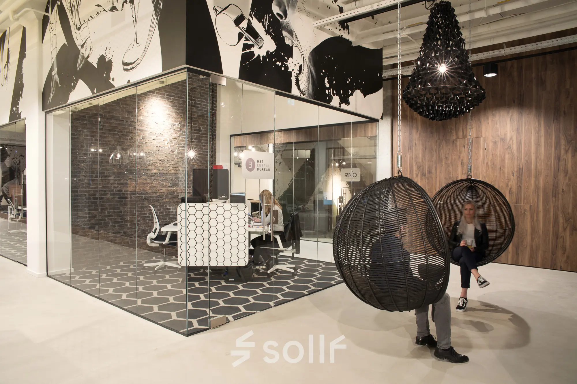 Moderne kantoorruimte huren in Eindhoven Strijp-S op Frederiklaan 10E met glazen wanden, stijlvolle meubels en decoratieve elementen. Personen voeren zakelijke activiteiten uit, zittend in designstoelen.