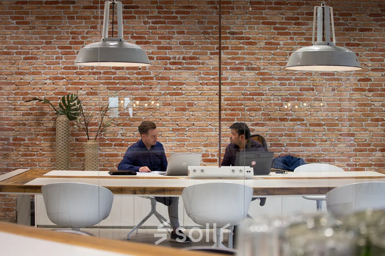 Twee mensen werken samen in een moderne kantoorruimte met bakstenen muur, houten tafel en witte stoelen, gelegen op Torenallee 20, Eindhoven Strijp-S.