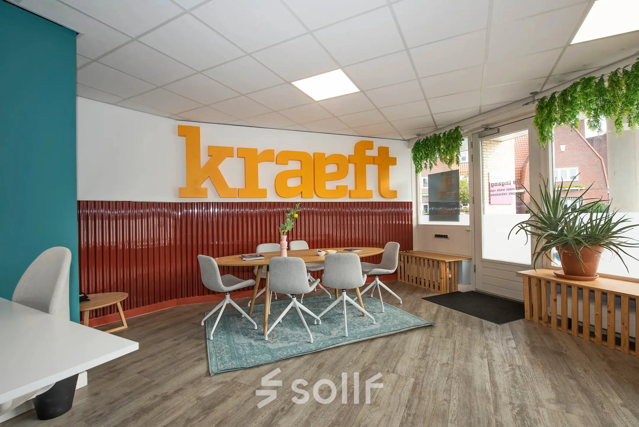 Moderne en ingerichte kantoorruimte aan de Boddenkampsingel 95 in Enschede met tafels, stoelen en planten. Grote oranje letters op de achtergrond en een comfortabele werkplek voor het huren van kantoren.