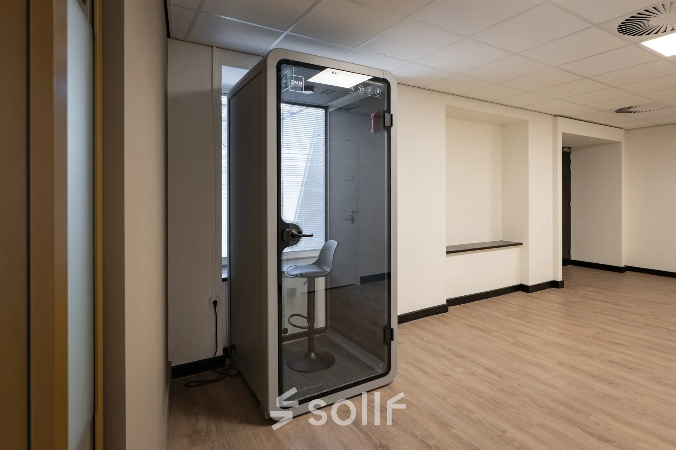 Kantoorruimte op Kuipersdijk 2-4 in Enschede met een moderne werkplekvoorziening en houten vloer. Het interieur is vrij minimalistisch met een stijlvolle telefoniecabine voor privégesprekken.