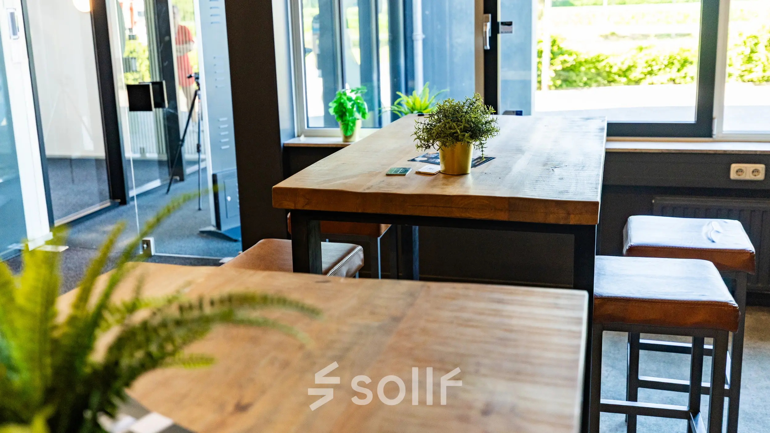 Moderne kantoorruimte in Enschede met houten tafels en hoge krukken bij grote ramen, voor een inspirerende werkplek in het kantoorpand op Marssteden 20. Ideaal voor kantoorruimte huren.