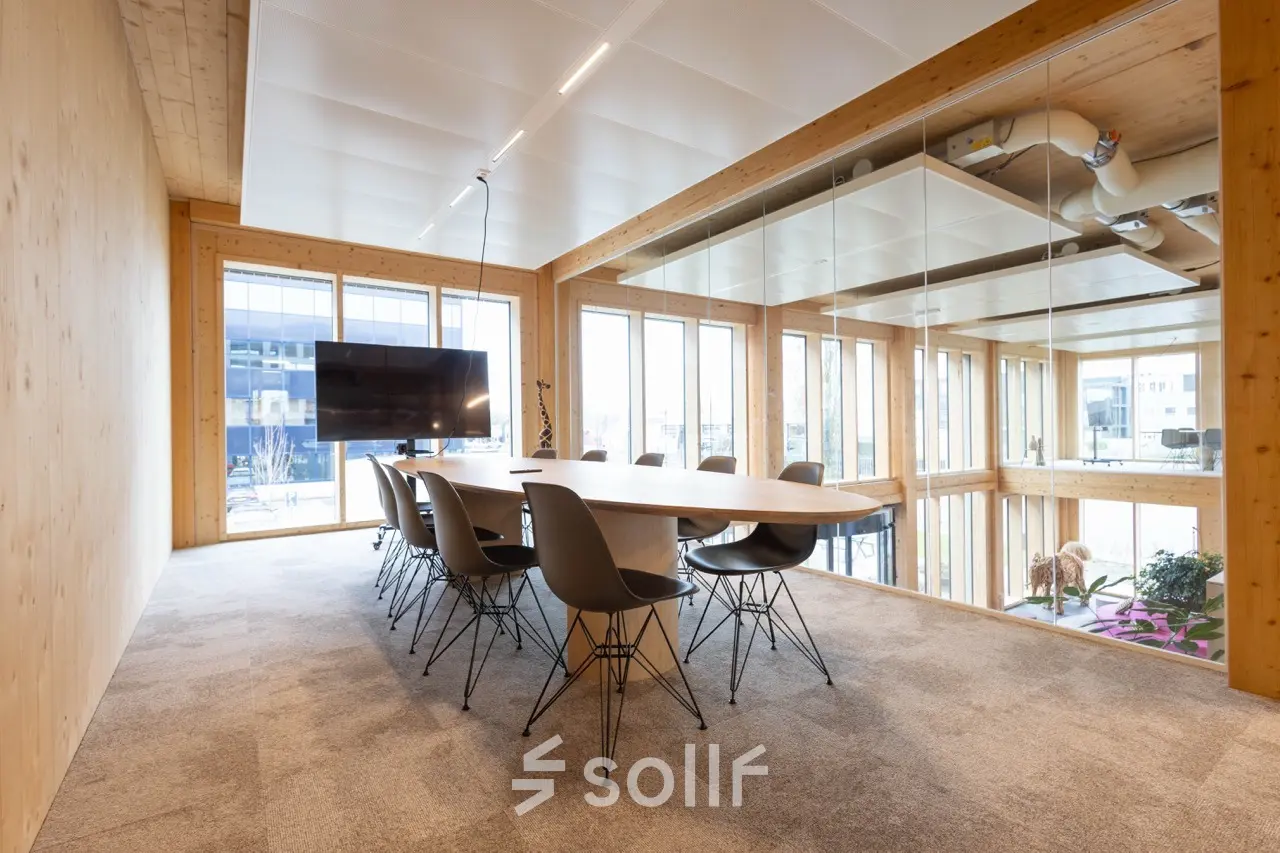 Moderne vergaderruimte in het kantoorpand op Moutlaan 1-23, Enschede, met grote ramen, houten afwerking en een grote tafel omgeven door stoelen. Perfect om een kantoorruimte te huren.