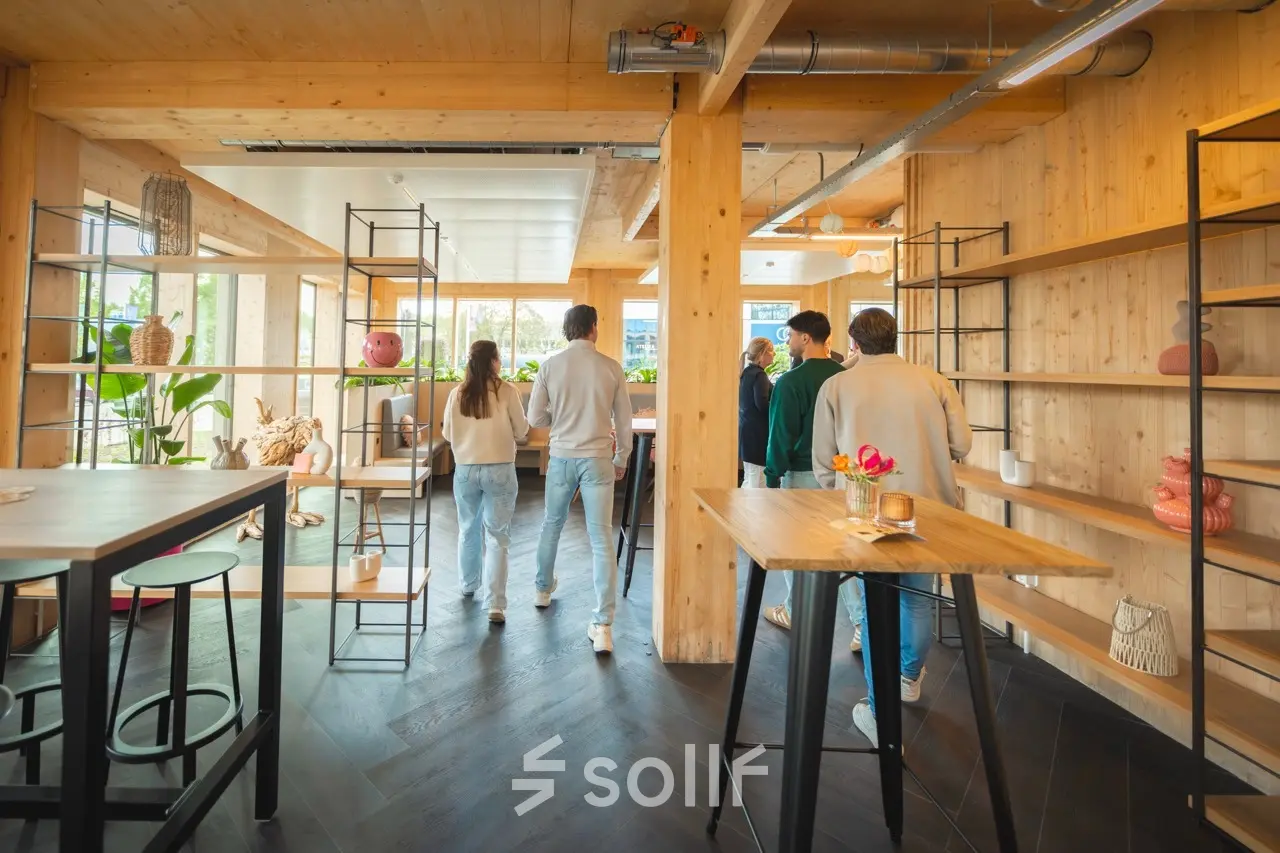 Moderne kantoorruimte huren op Moutlaan 1-23, Enschede, met een lichte inrichting en houten elementen. Mensen voeren zakelijke activiteiten uit in een gemeubileerd interieur.