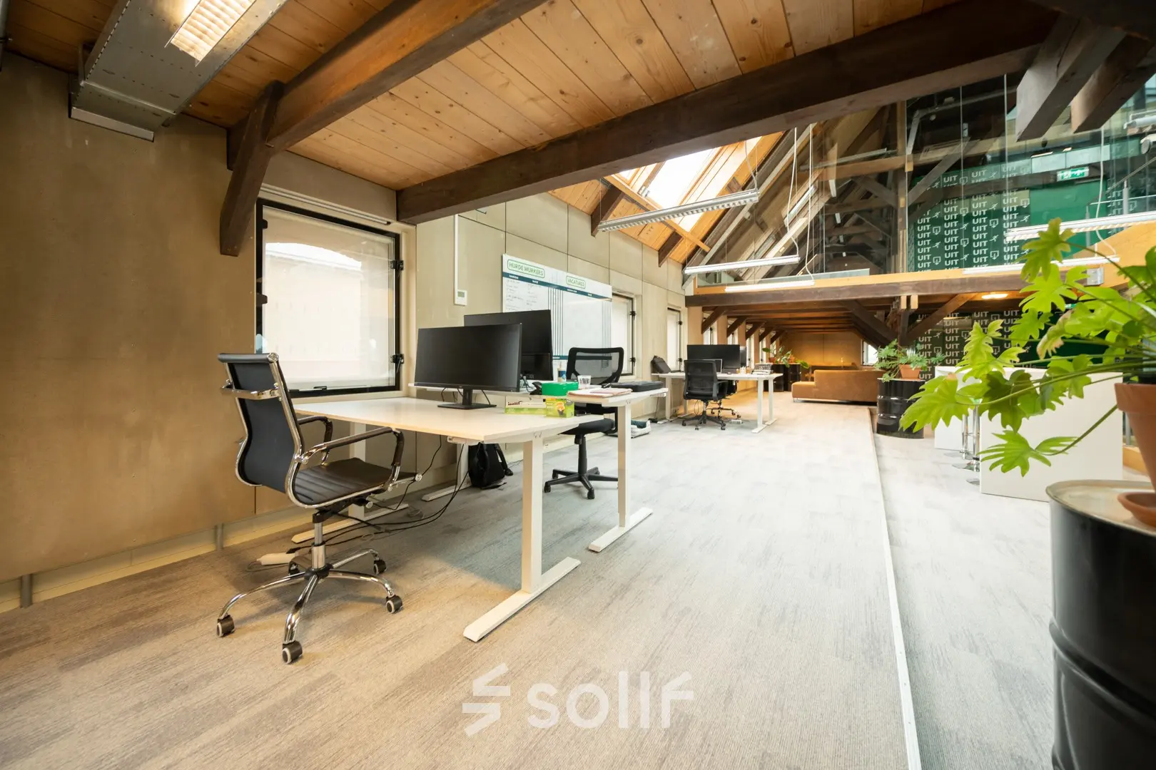 Kantoorruimte huren in Franeker aan de Prins Hendrikkade 3 met een moderne, open indeling. Voorzien van werkstations met bureaustoelen en computerschermen onder een rustiek houten plafond.