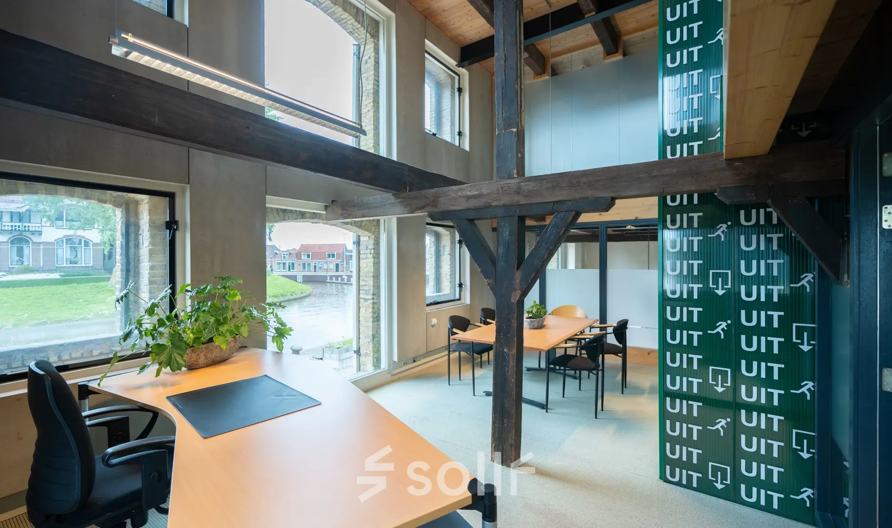 Kantoorruimte op de eerste verdieping van een kantoorpand aan Prins Hendrikkade 3 in Franeker, voorzien van houten balken, grote ramen, en diverse werkplekken met bureaus en stoelen.