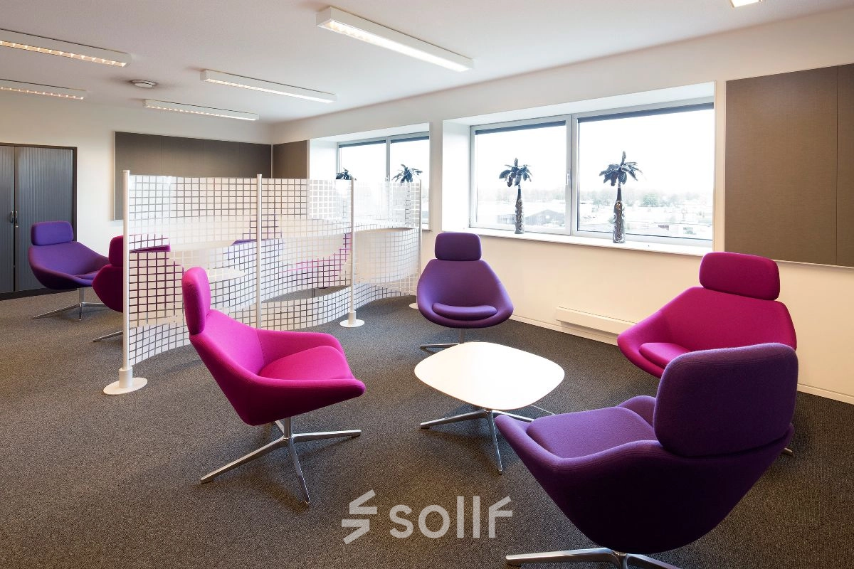 Kantoorruimte huren in Geleen met moderne paarse stoelen en bijzettafels, natuurlijk licht door grote ramen, ideaal voor een ontspannen werkomgeving.