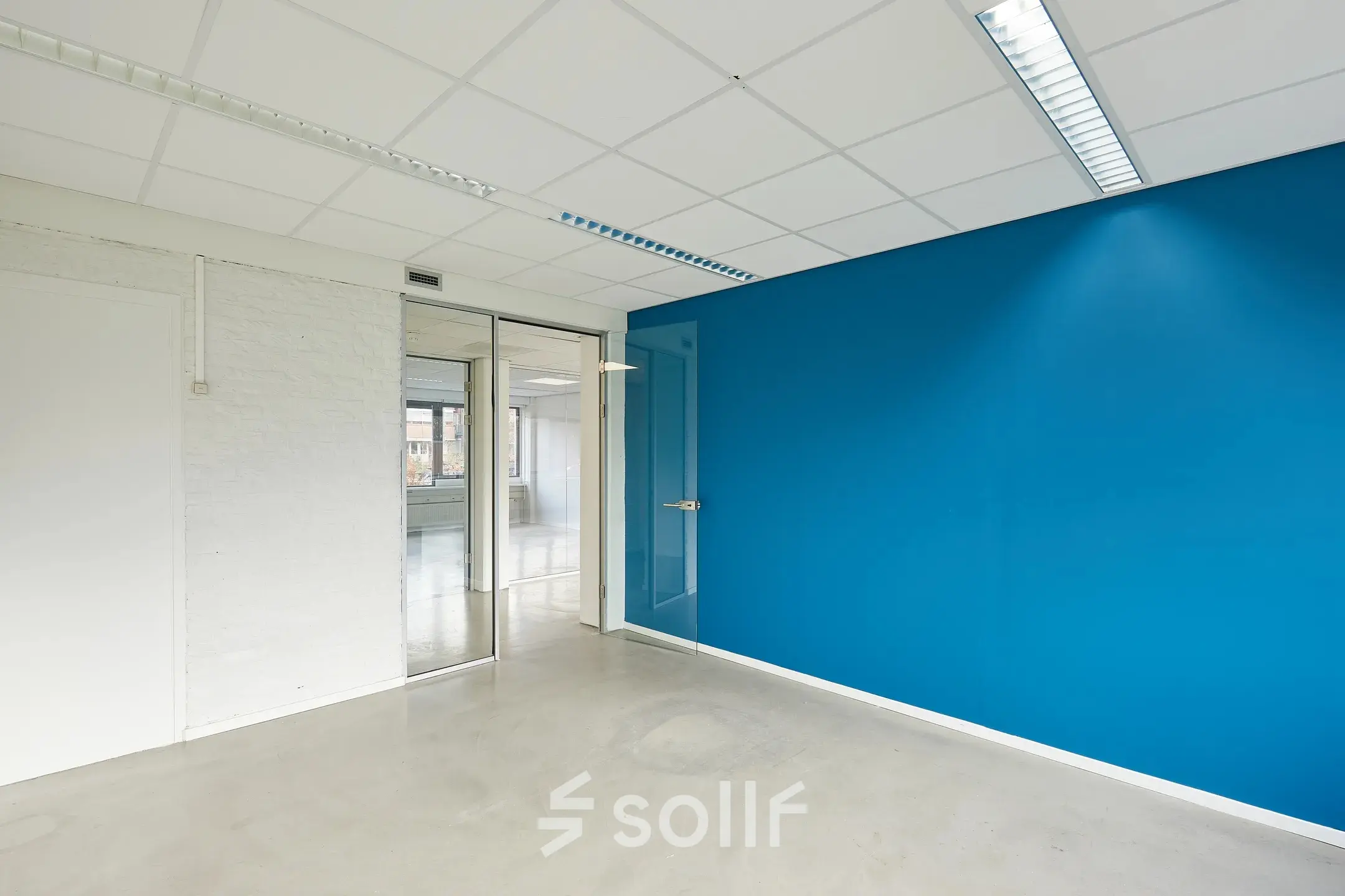 Lege kantoorruimte met een heldere blauwe muur, strakke betonnen vloer en glazen deuren in het kantoorpand op Schweitzerlaan 12, Groningen. Ideaal voor wie een moderne kantoorruimte wil huren.