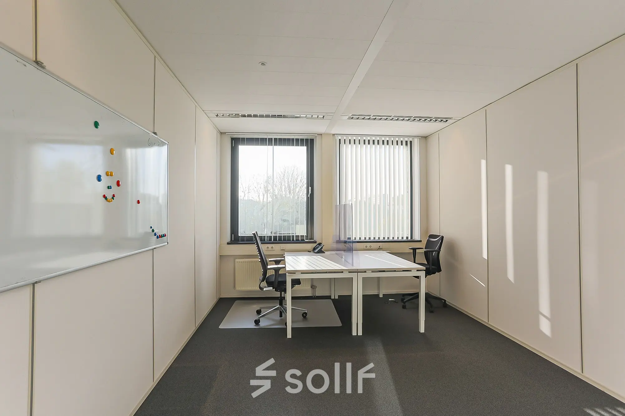 Lichte kantoorruimte met een wit bureau en twee zwarte stoelen, witte muren en een groot raam met verticale lamellen op Zernikepark 12, Groningen.