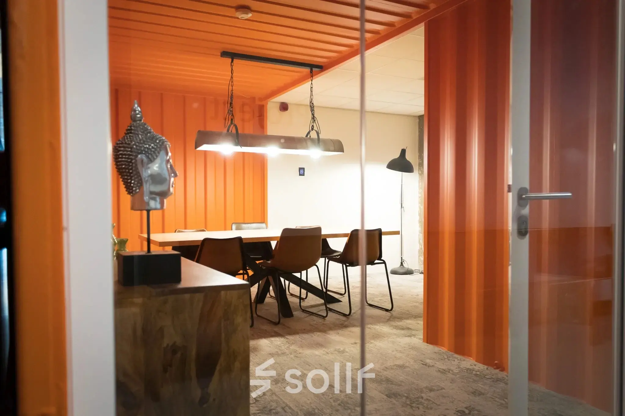 Moderne kantoorruimte huren in Haarlem Waarderpolder met glazen deur, stoere oranje muren en vergadertafel met stoelen, ideaal voor team meetings of creatieve sessies.