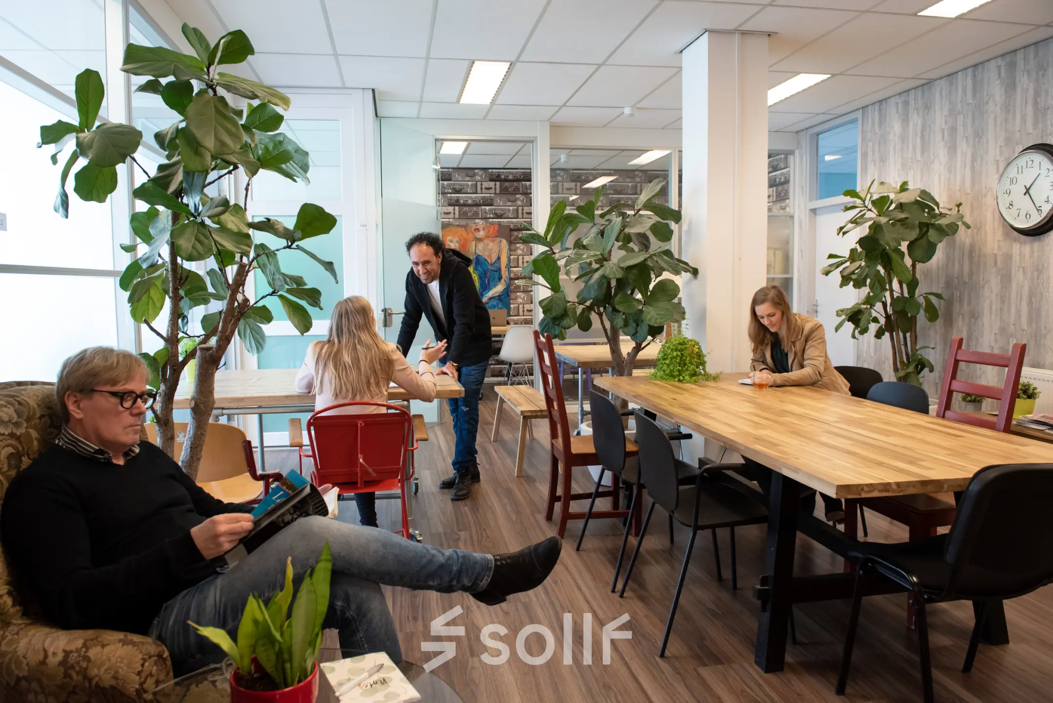 Kantoorruimte huren in Haarlem Waarderpolder op Waarderweg 19, met gezellige werkplekken en moderne meubels. Drie mensen werken geconcentreerd aan tafels omringd door planten, wat een inspirerende sfeer geeft.