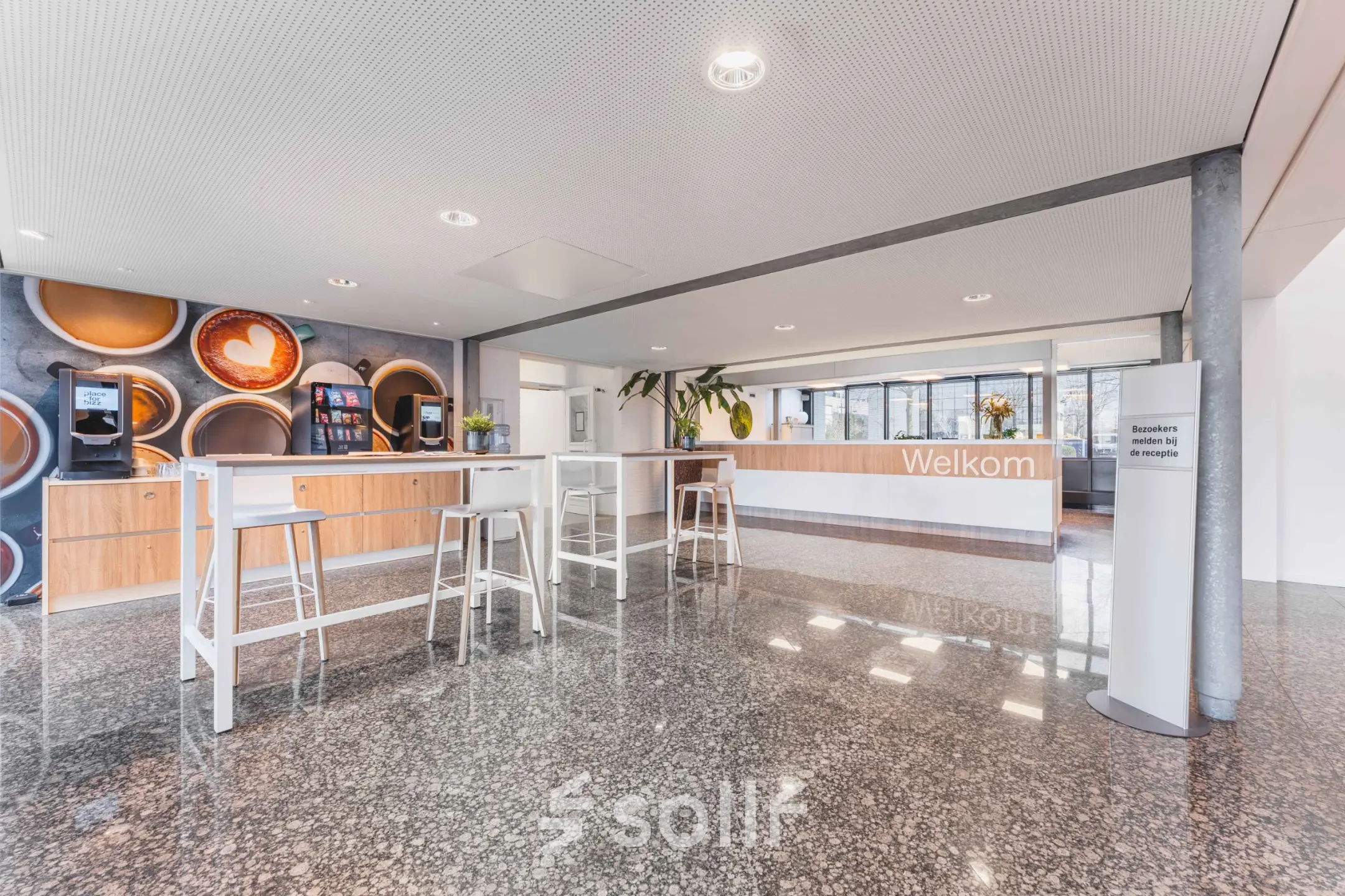 Lichte en ruime receptie met moderne houten balie en hoge tafels, geschikt voor informele ontmoetingen. Perfecte locatie voor kantoorruimte huren aan Steenovenweg 5 in Helmond.